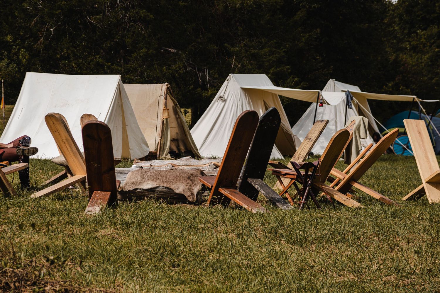 Historical reenactment campsite with white canvas tents and period equipment set up on grassy field.