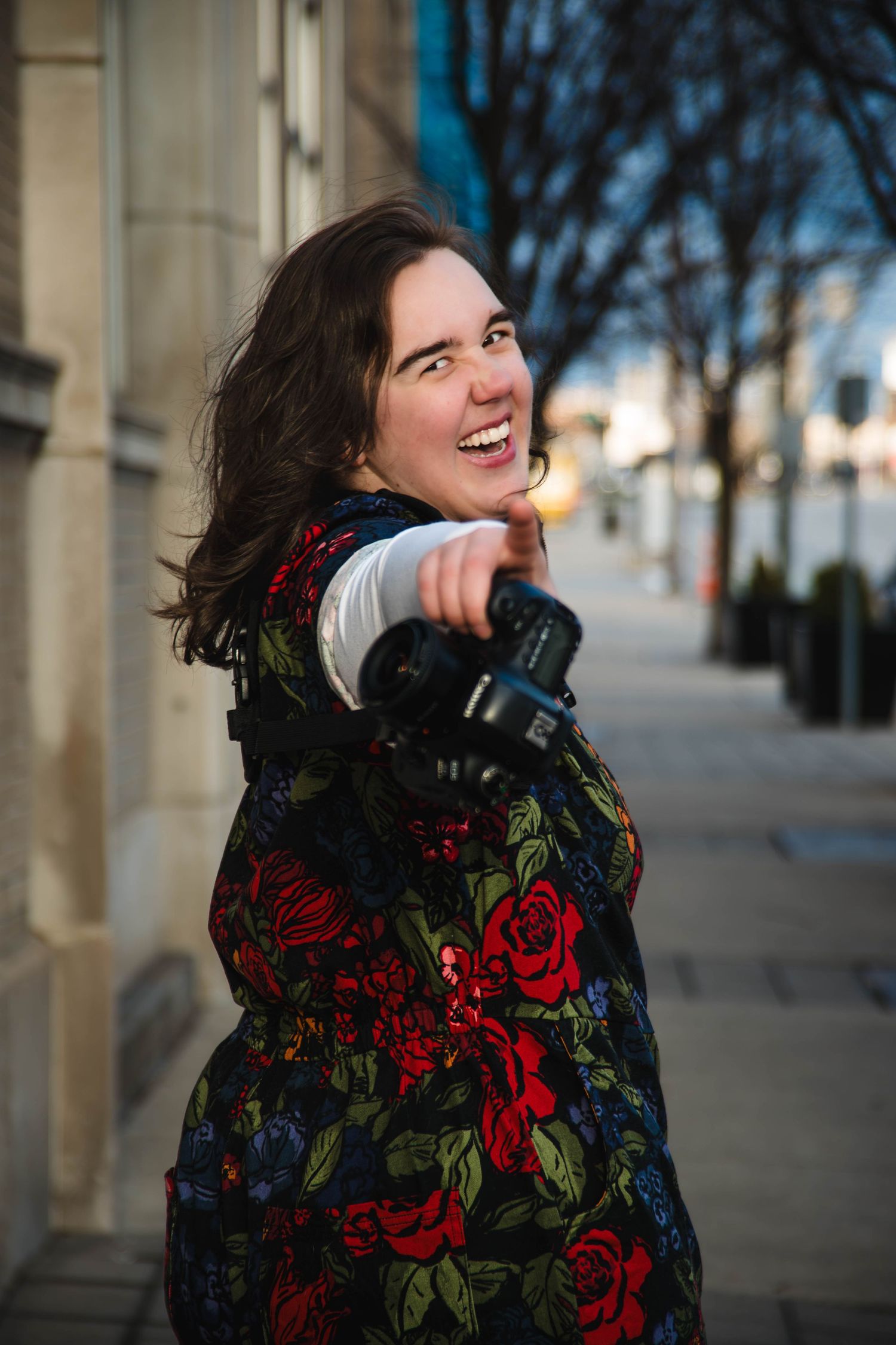 Person wearing a floral patterned coat with red roses laughs joyfully in an outdoor urban setting.