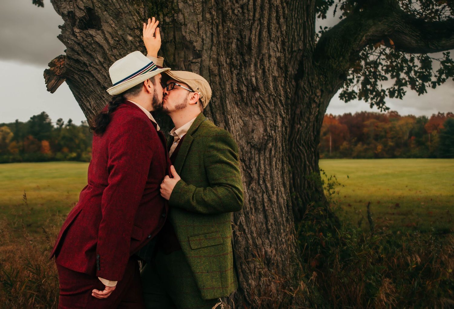 A romantic couple in autumn attire shares tender moments in a field during golden hour with fall foliage in background.