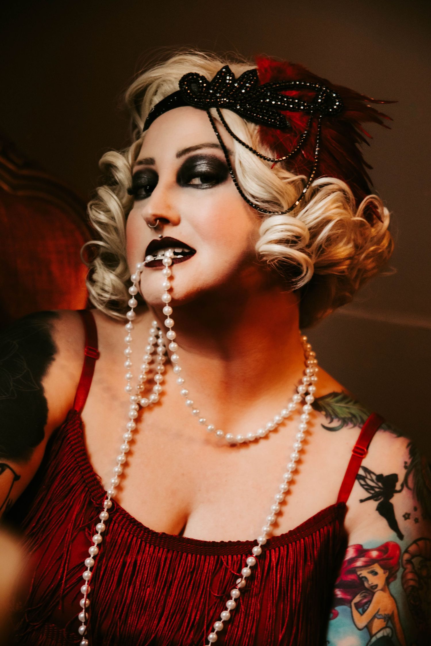 A dramatic burlesque-style portrait series featuring pearls, red fringe, dark feathers and dramatic makeup in moody lighting.
