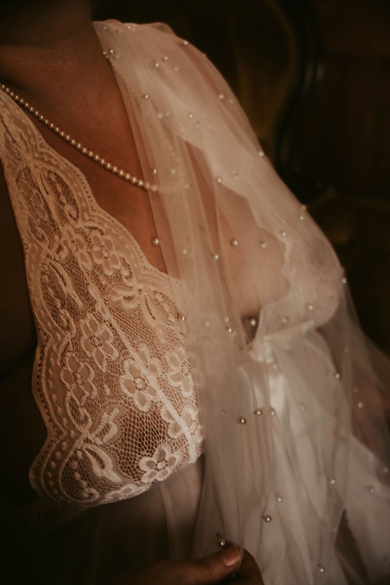 Close-up details of delicate white lace and beading on a flowing wedding dress veil against dark background.
