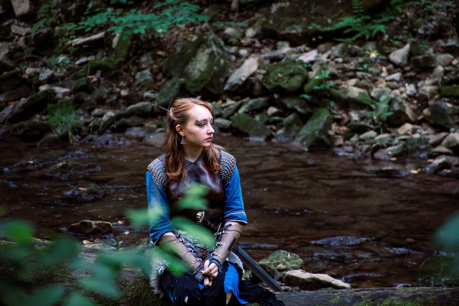 Person exploring a shallow creek bed surrounded by lush green forest vegetation and fallen leaves.