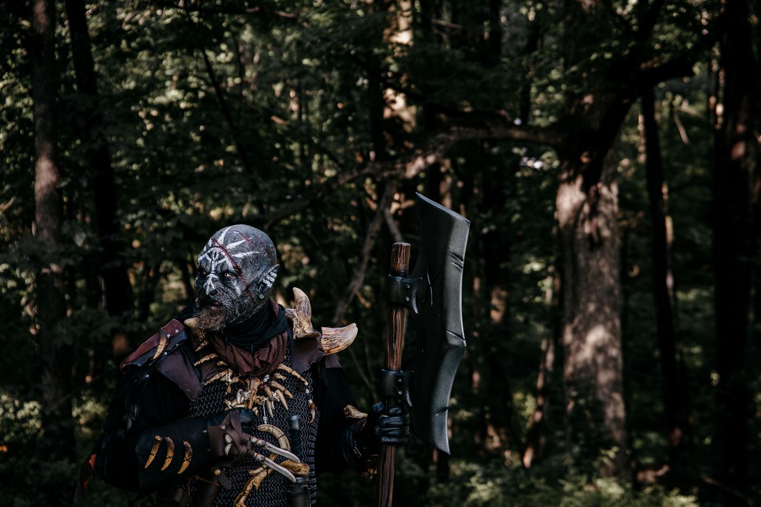 A costumed archer in dark fantasy armor stands in a dense forest holding a compound bow.