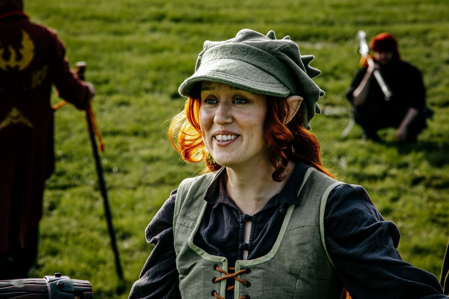 Smiling woman in medieval costume with green hat and vest at outdoor Renaissance faire event.
