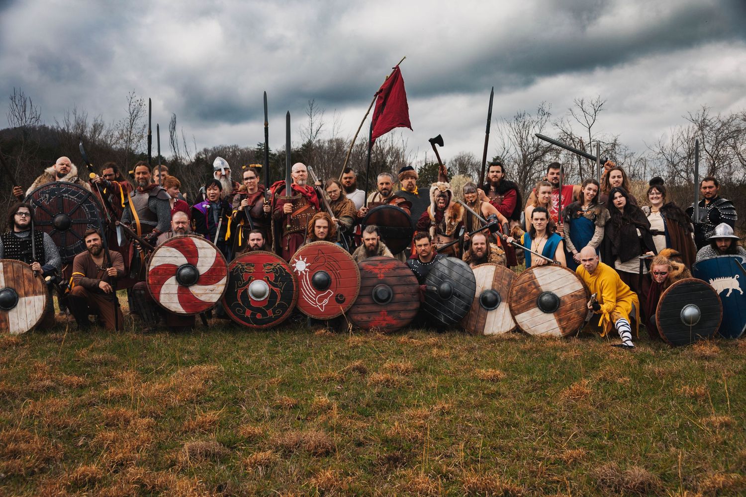 A group of medieval reenactors in Viking costumes pose with shields and weapons on a grassy hillside at dusk.