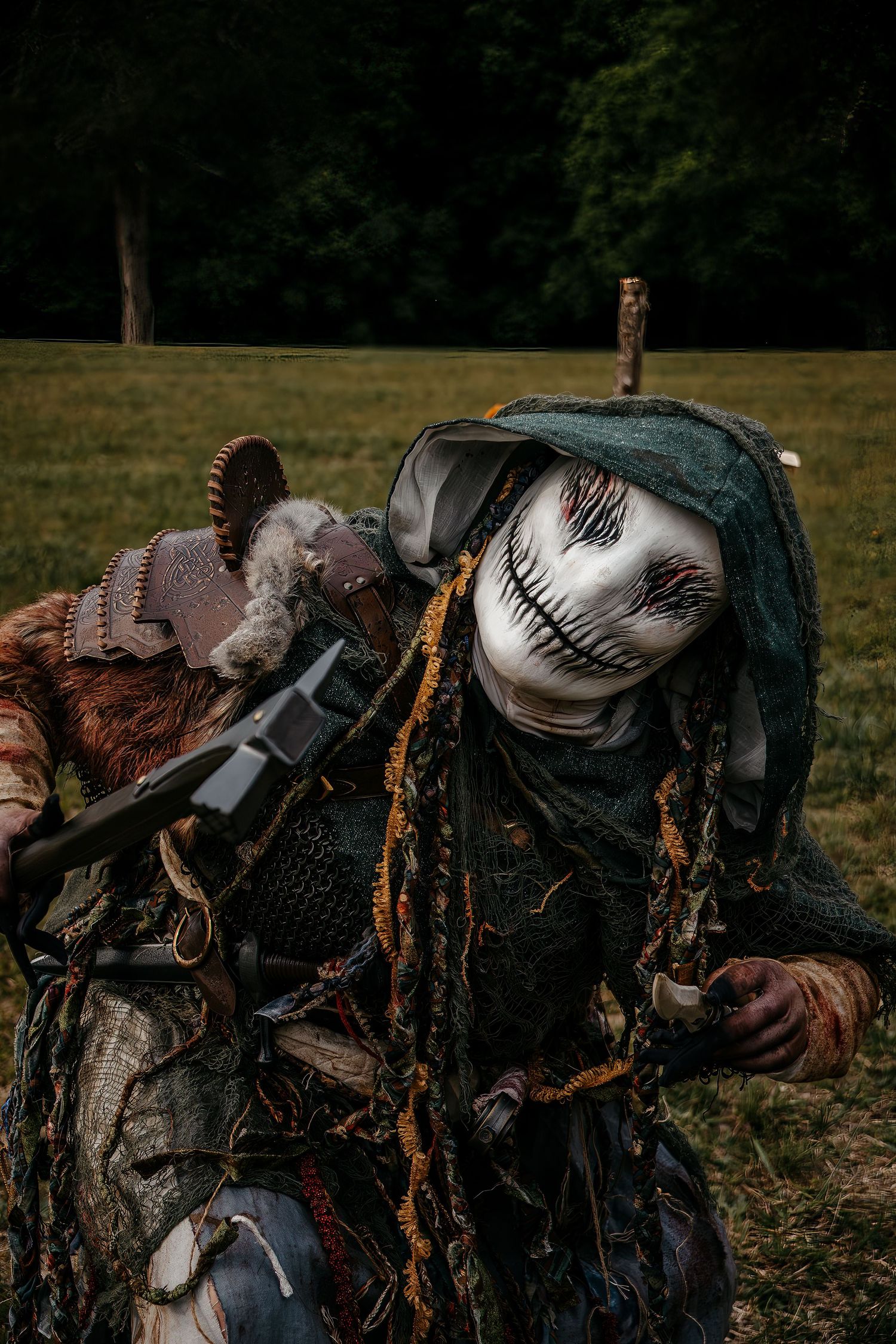 Creepy scarecrow costume with white face paint, tattered robes, and dark accessories in an outdoor field setting.