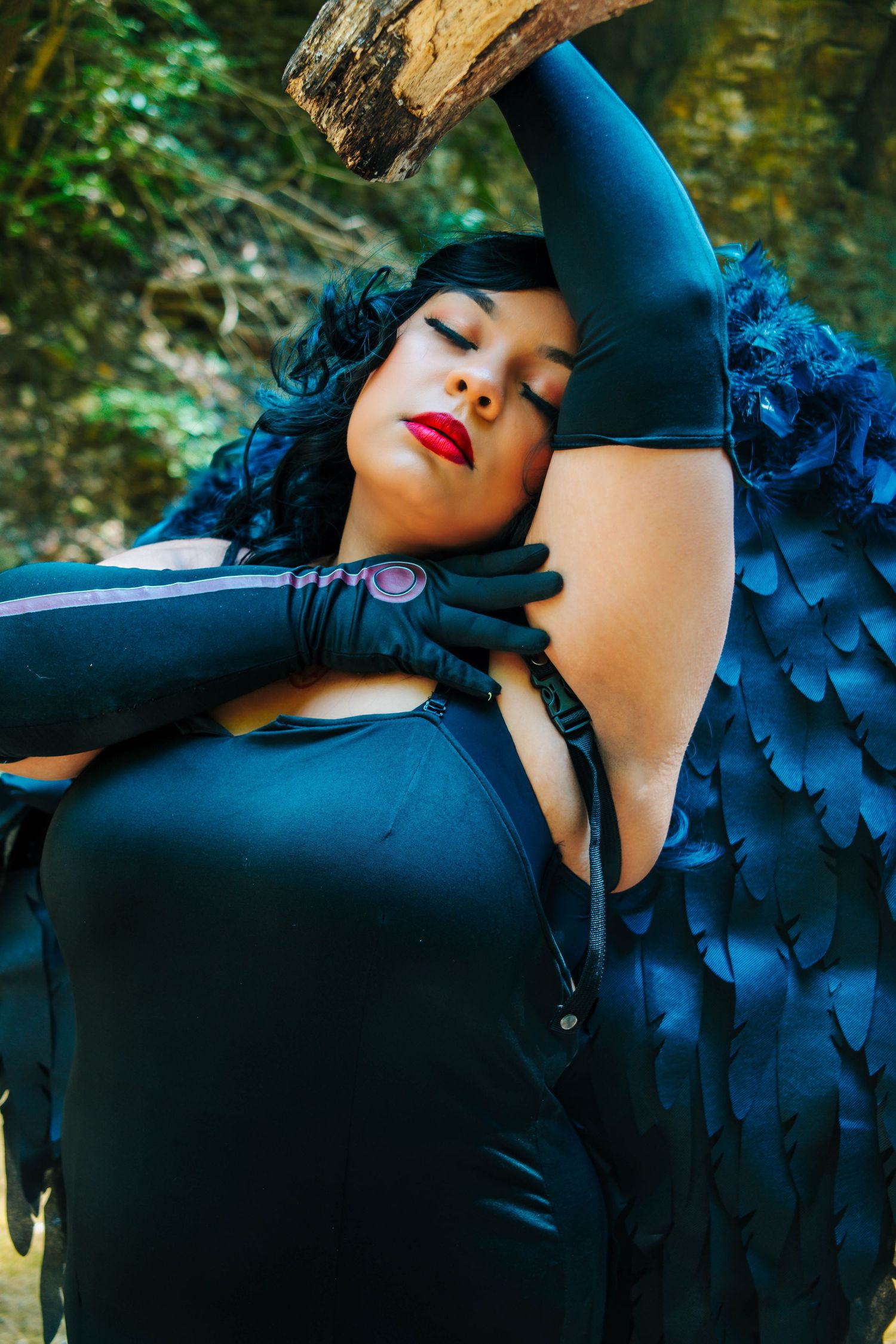 Artistic fashion portrait in black attire with dramatic lighting and dark floral details against a forest backdrop.