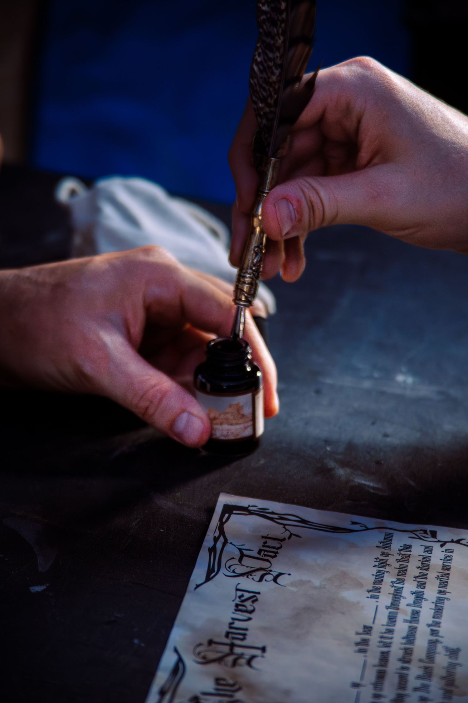 A hand uses a fountain pen to write calligraphy on parchment paper against a dark background.