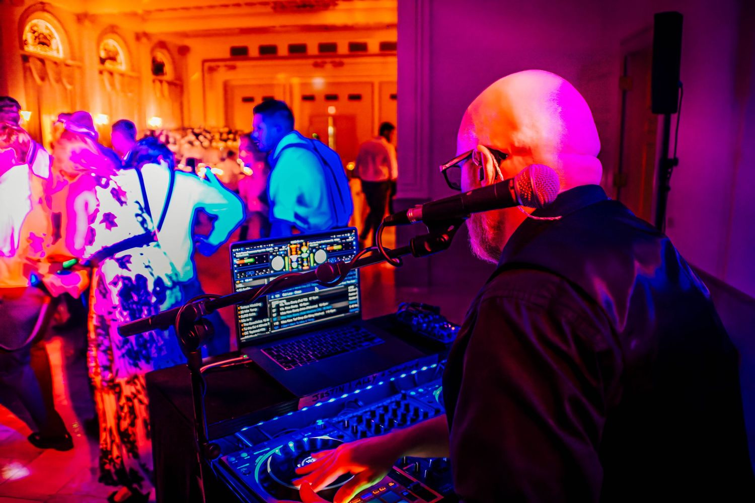 Colorful nightclub scene with purple and pink lighting illuminating DJ equipment and dance floor atmosphere.