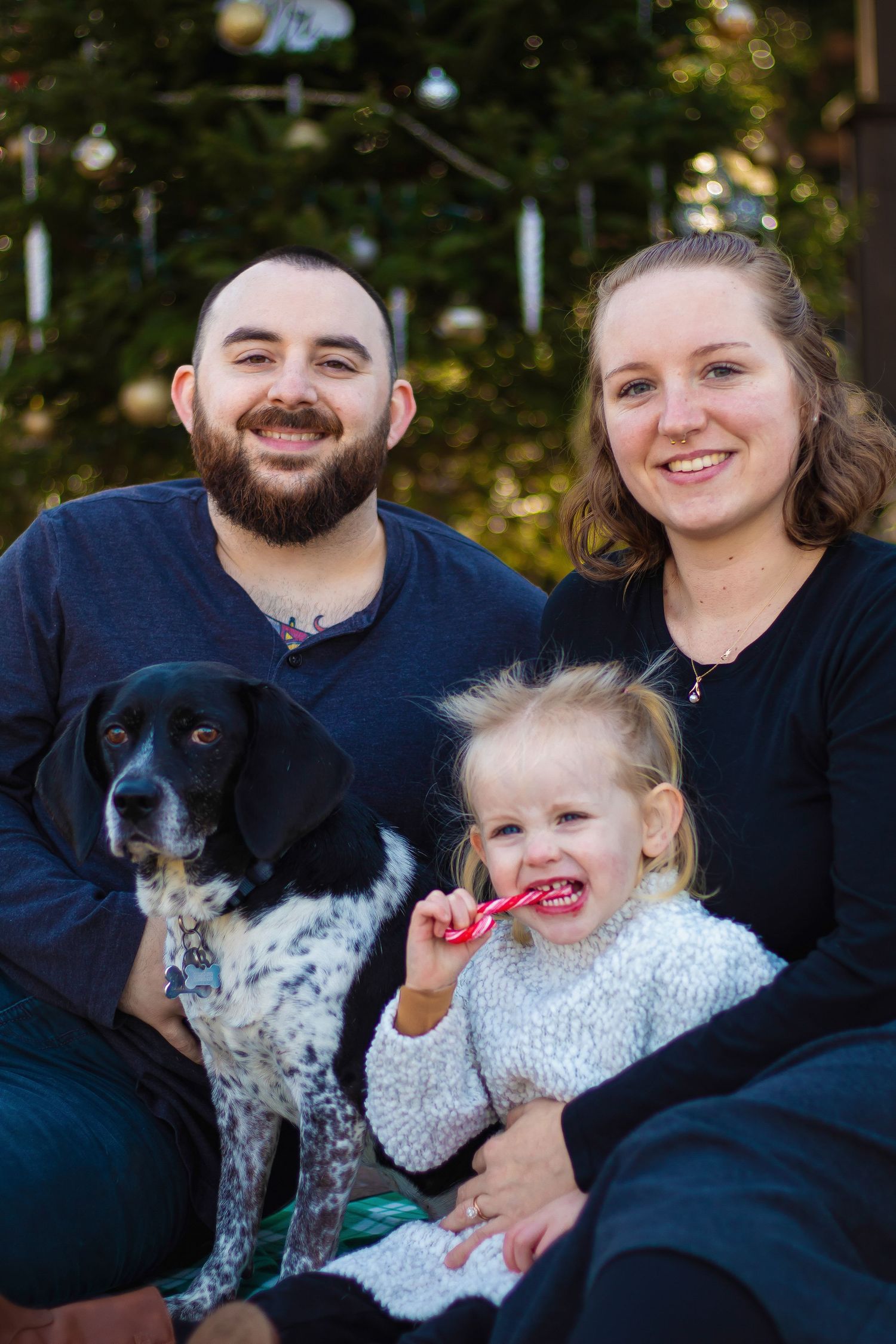 Family portrait with dogs and young child wearing casual attire outdoors.