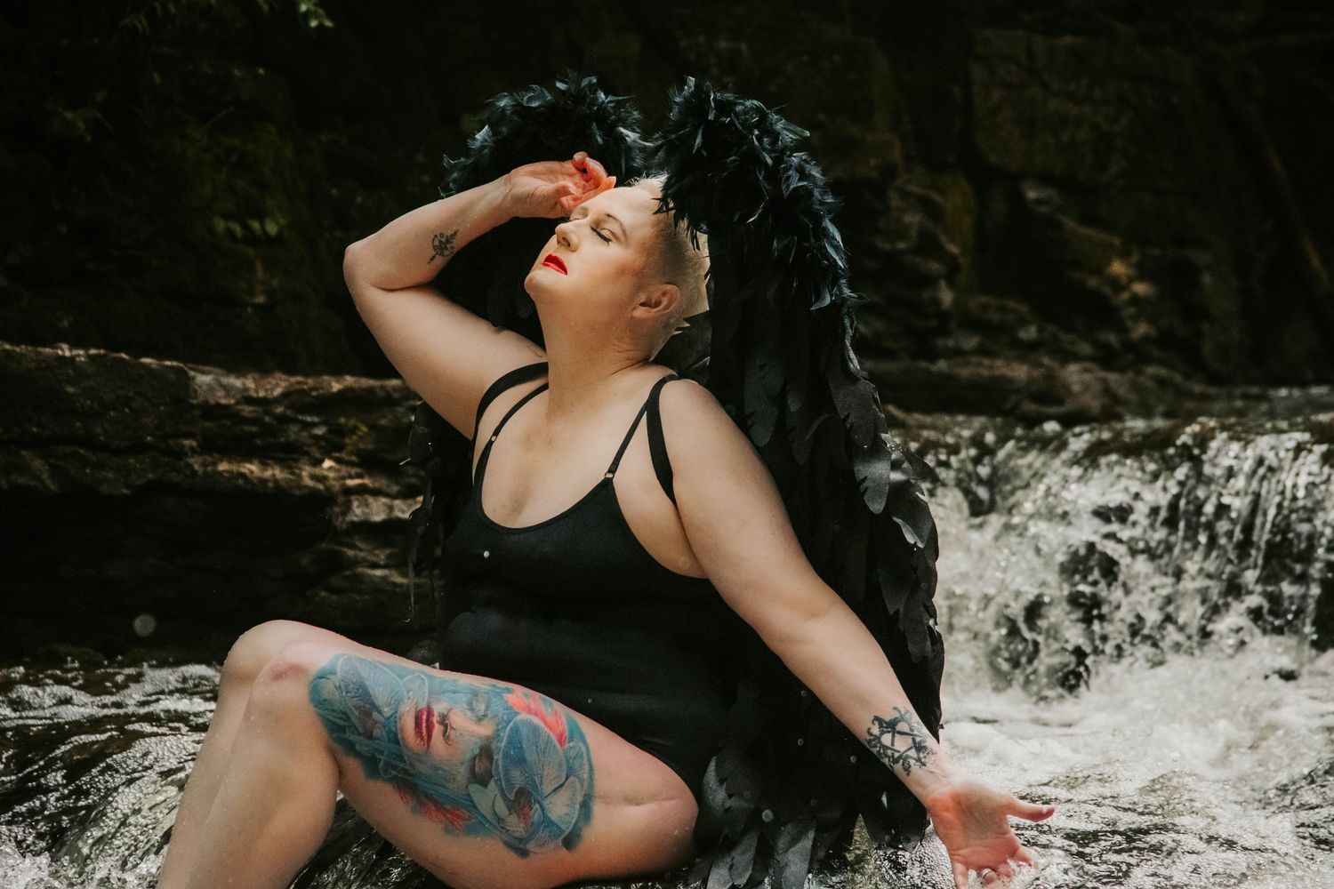 Woman in black swimwear poses near cascading waterfall.