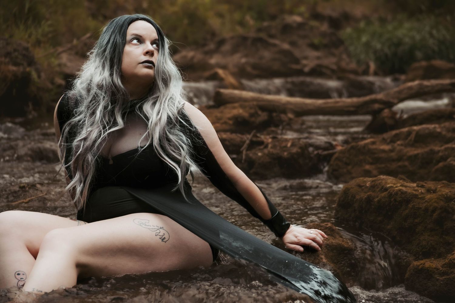 Dramatic outdoor portrait with flowing black dress against earthy backdrop.
