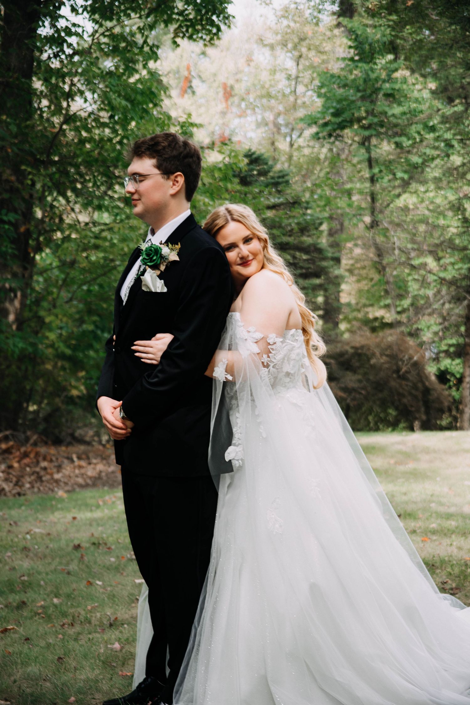 Romantic wedding couple embraces in a lush garden setting with sunlight filtering through trees.
