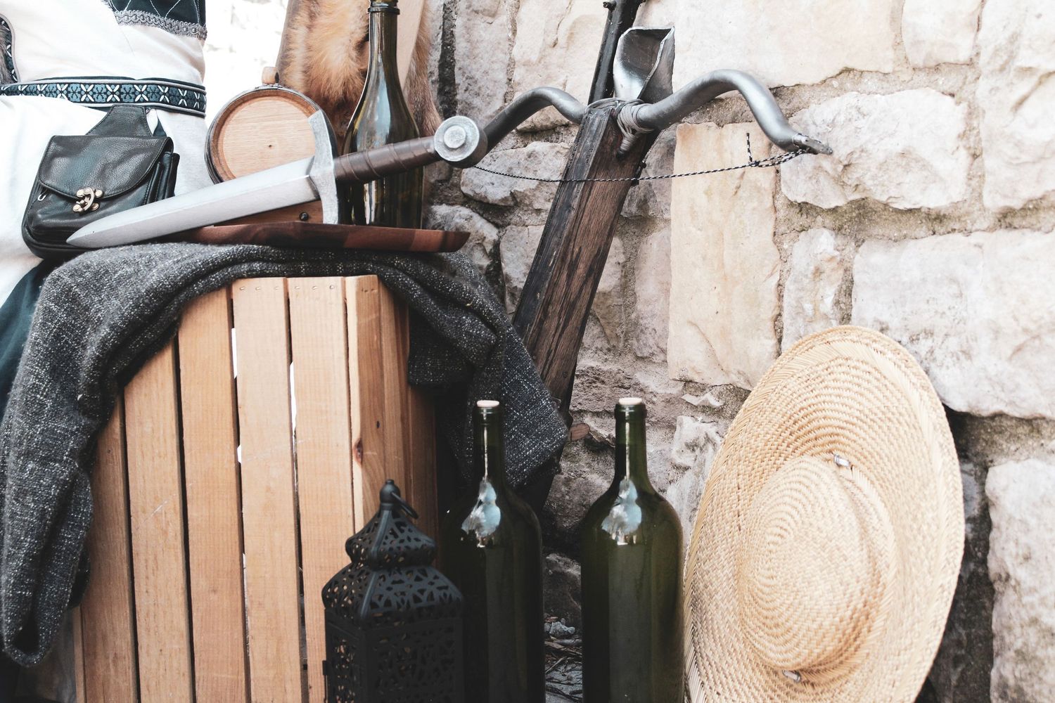Rustic wooden barrels stacked against stone walls in a traditional wine cellar with straw hats on display.