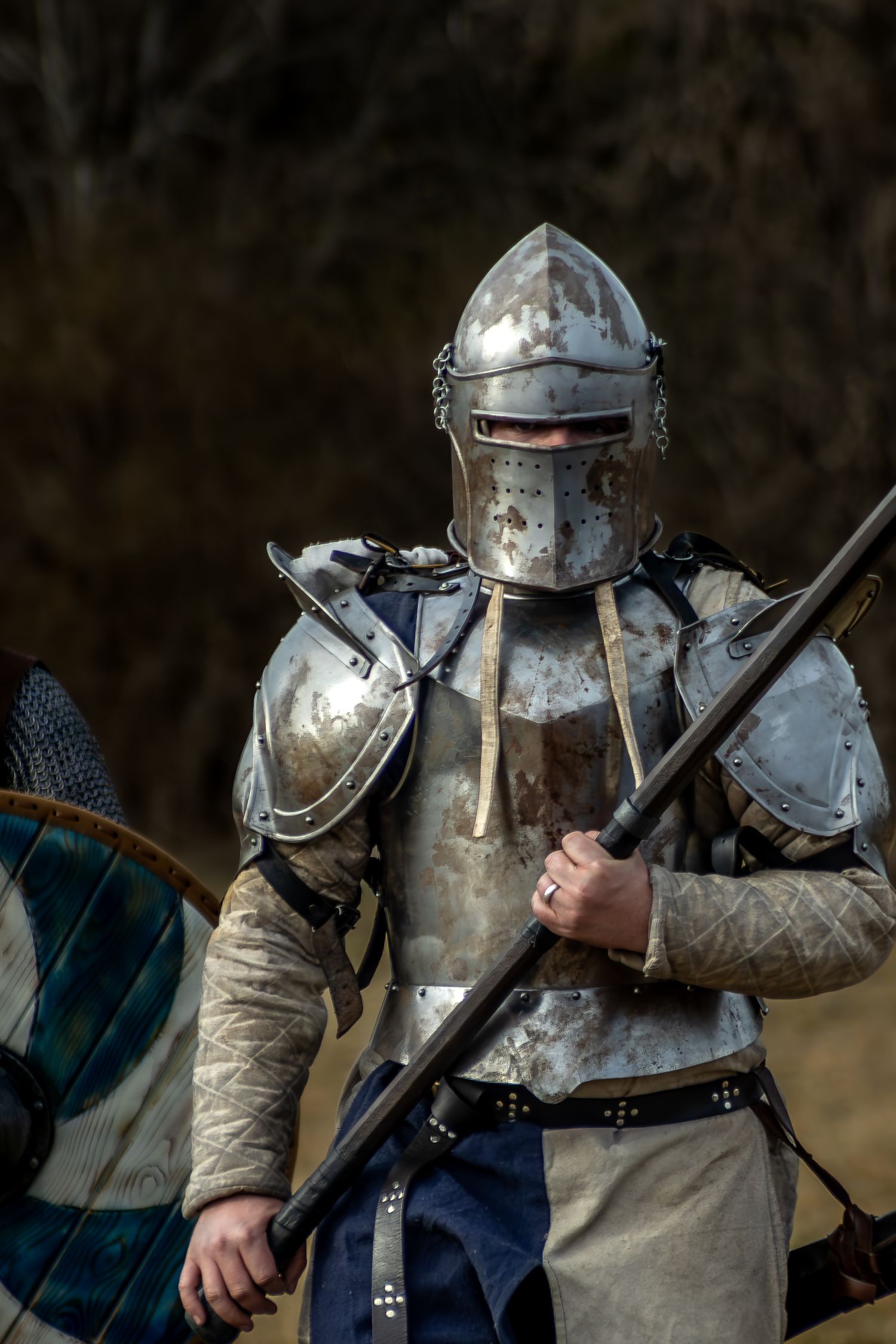 Medieval knight in full plate armor and helmet holding a lance during a historical reenactment.