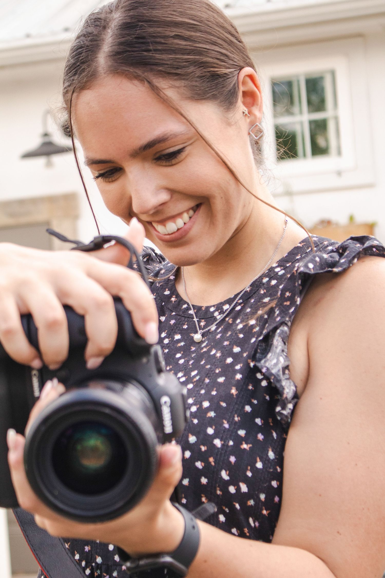 A photographer in a polka dot dress smiles while looking through a professional DSLR camera lens.