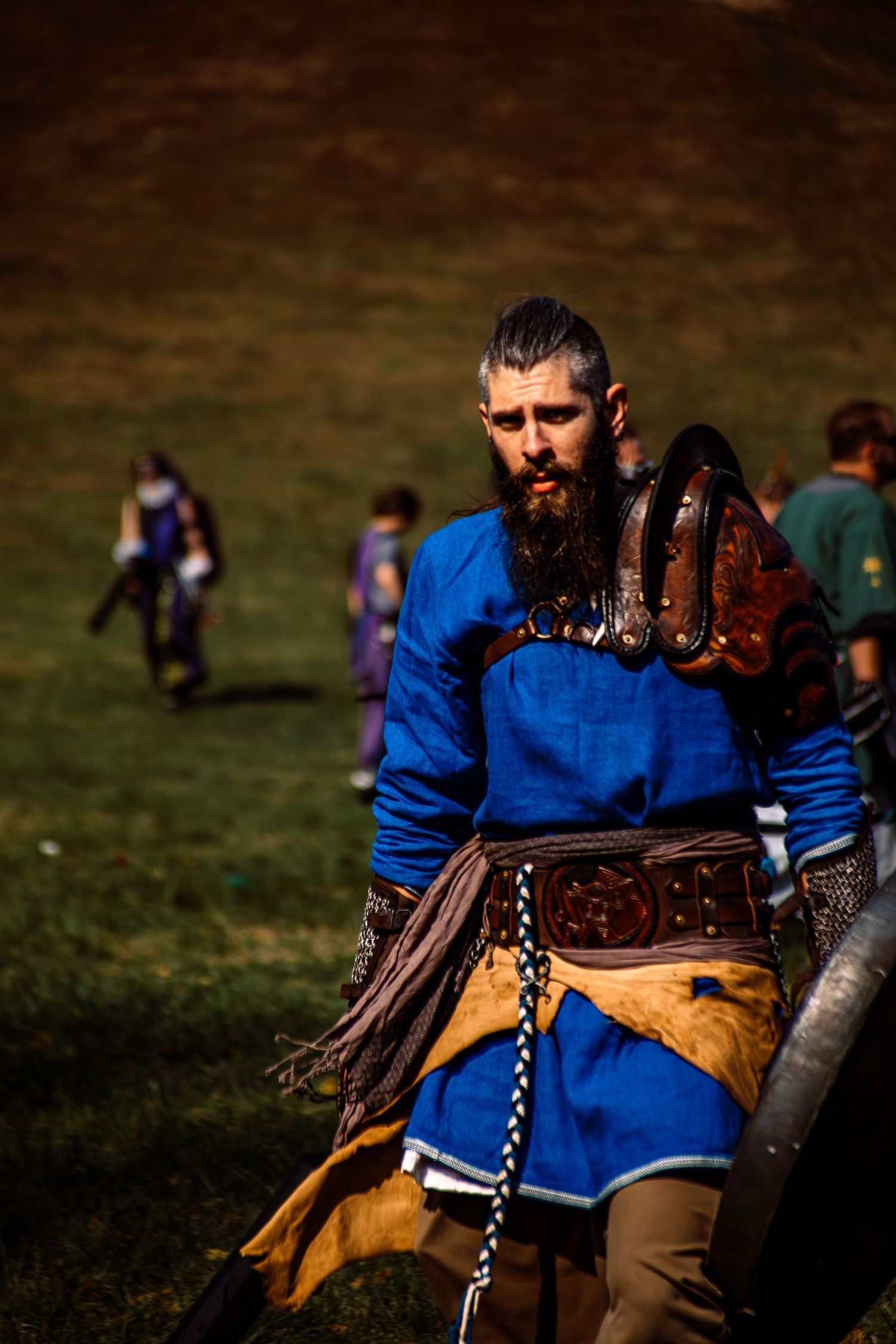 Reenactor in blue medieval tunic and armor sits during historical event.