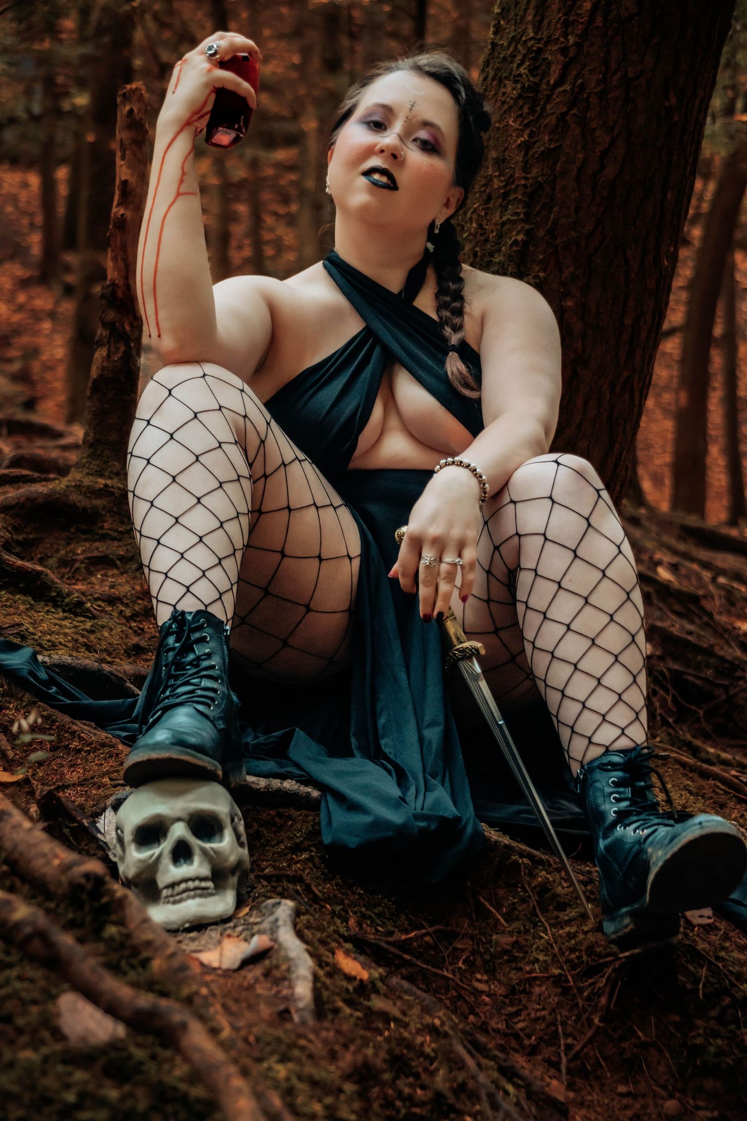 Gothic photoshoot in dark forest featuring fishnet stockings, combat boots, and decorative skull prop.