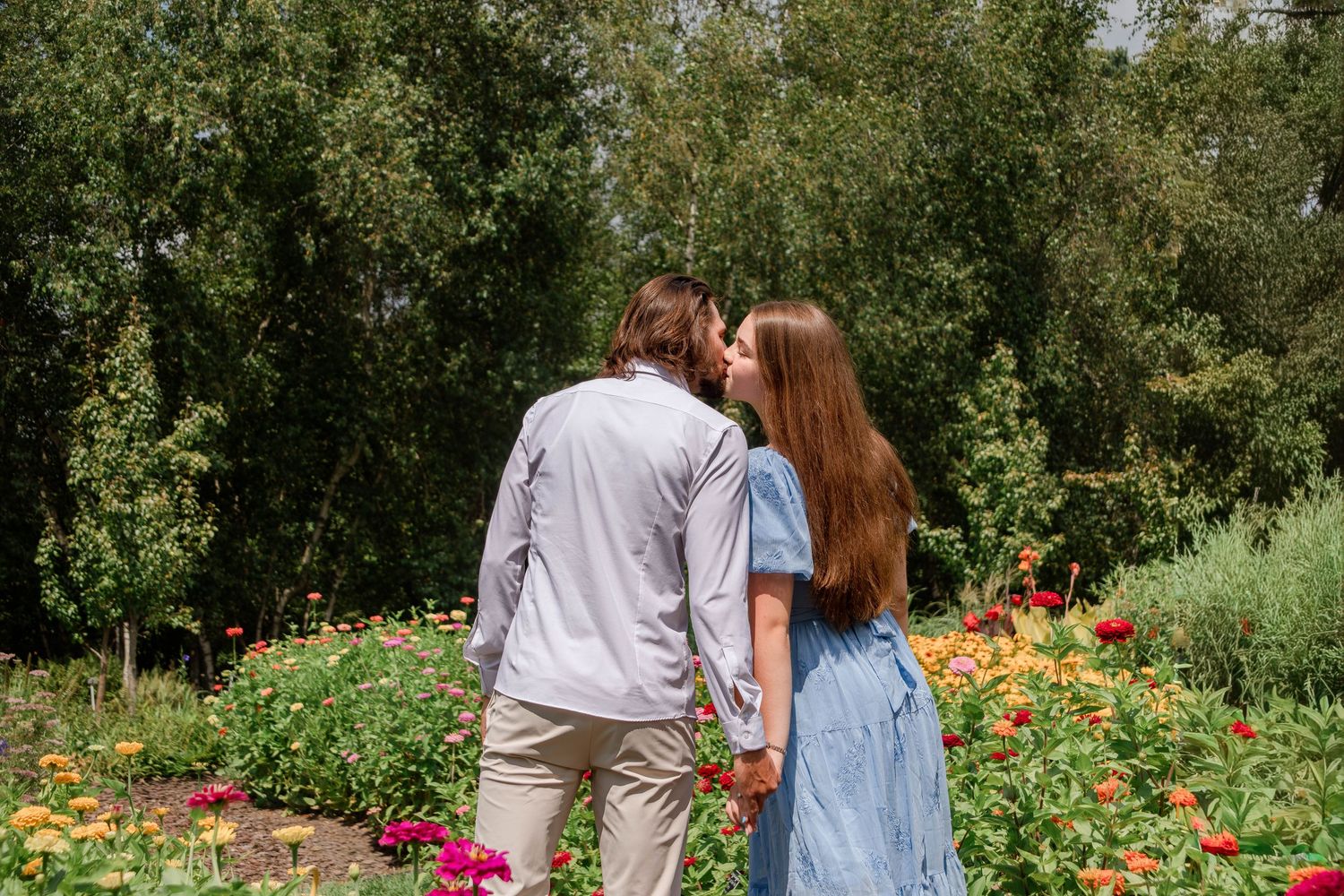 A couple walks through a garden with vibrant orange and pink flowers in bloom.