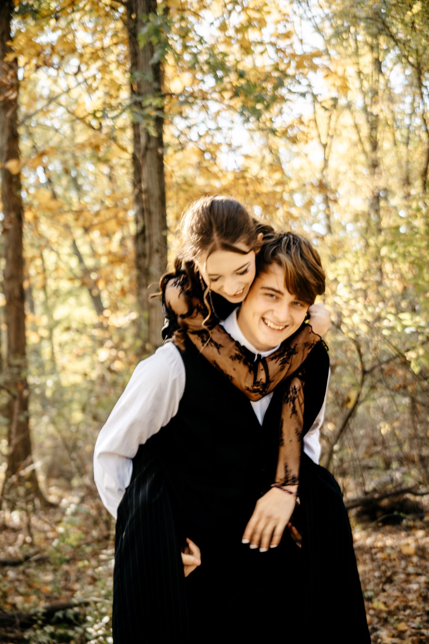 Two people in vintage-inspired outfits share a playful moment in a wooded autumn setting.