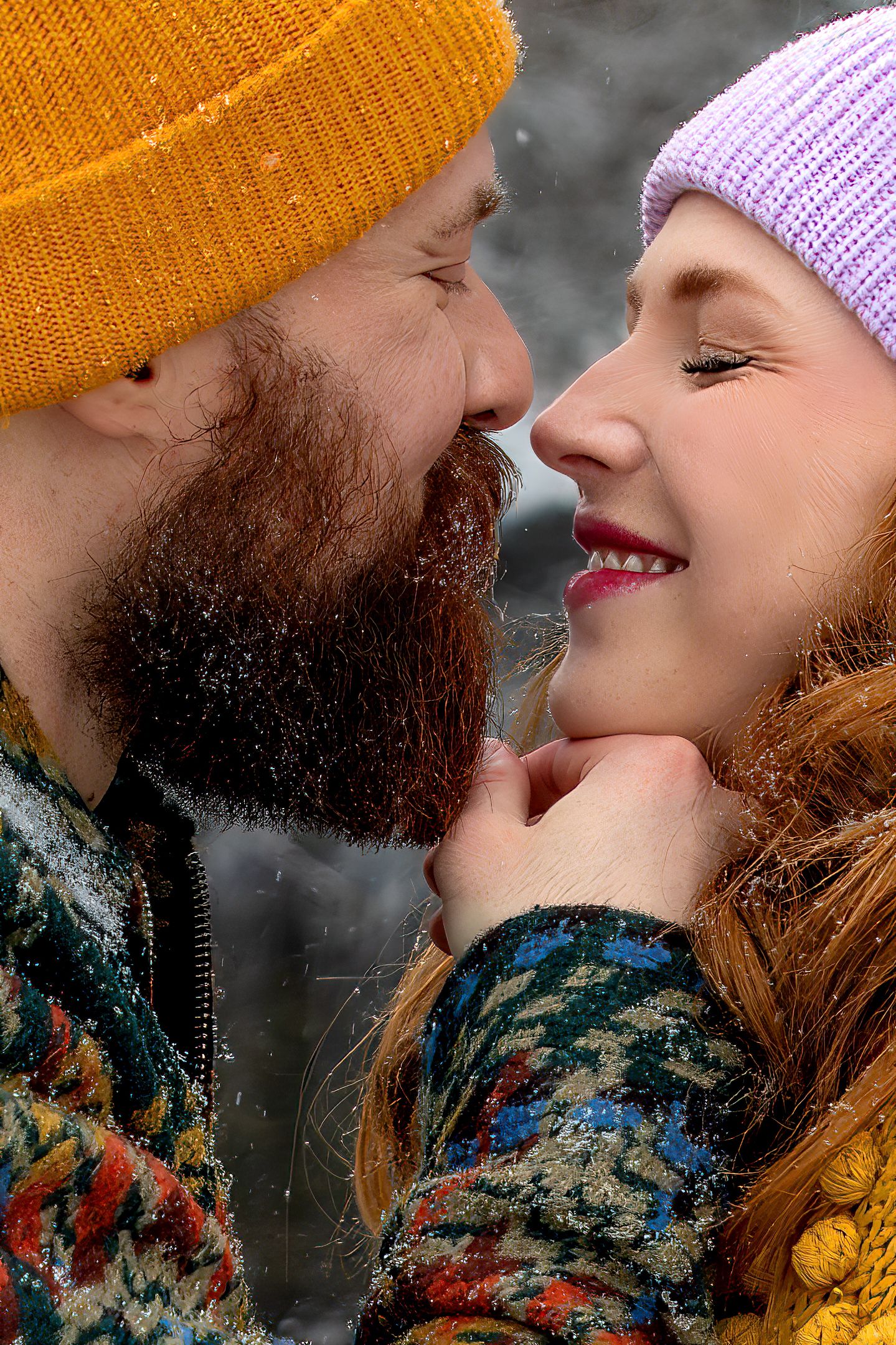 A romantic winter scene showing two people in knit hats sharing an intimate moment against a dark background.