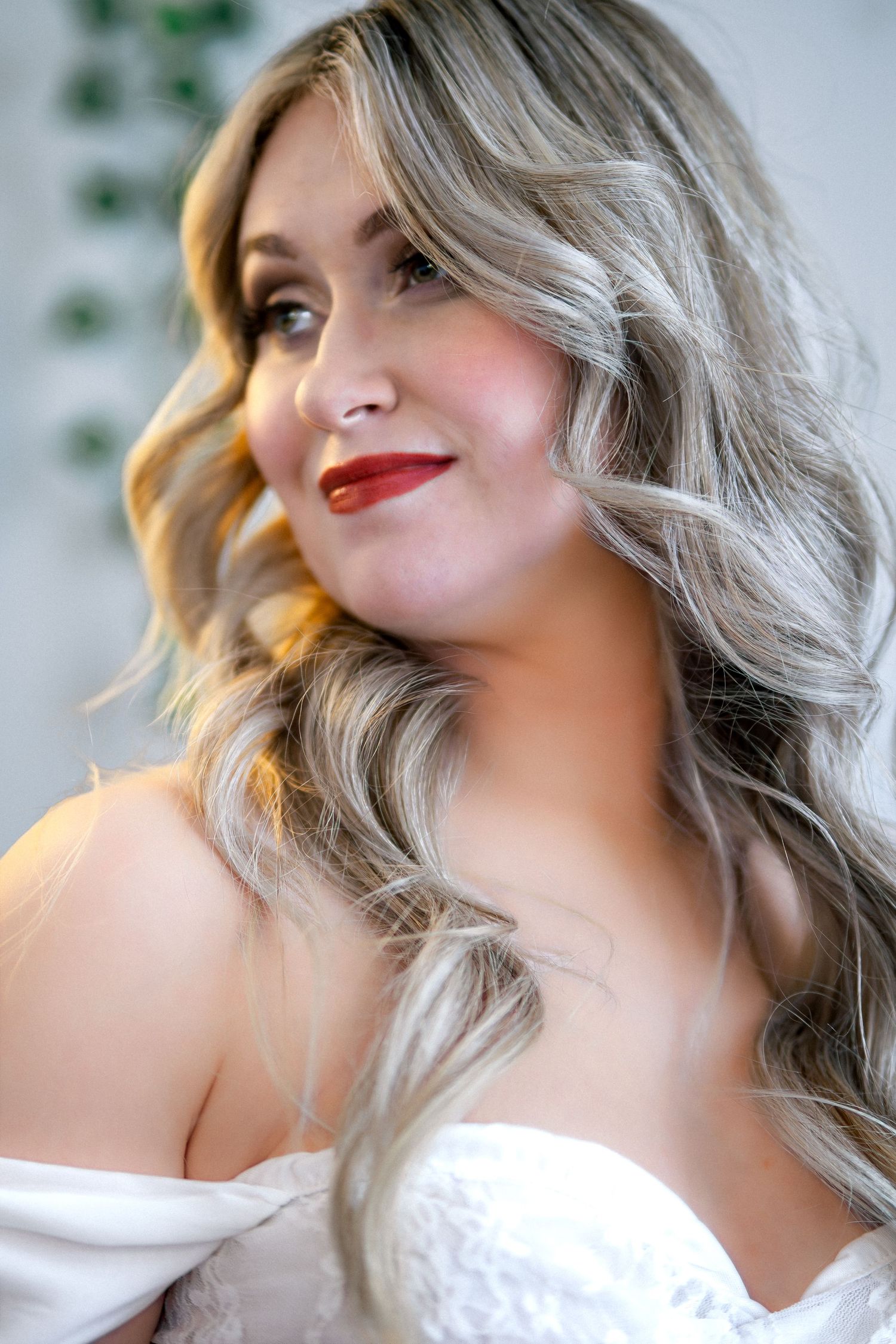 A woman with wavy silver-blonde hair and red lipstick poses in a white top against a light background.
