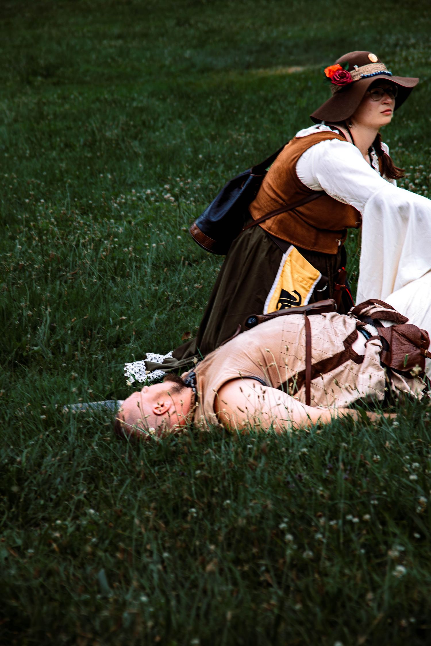 A person in a brown hat and white dress lies peacefully on green grass in a vintage-style photograph series.