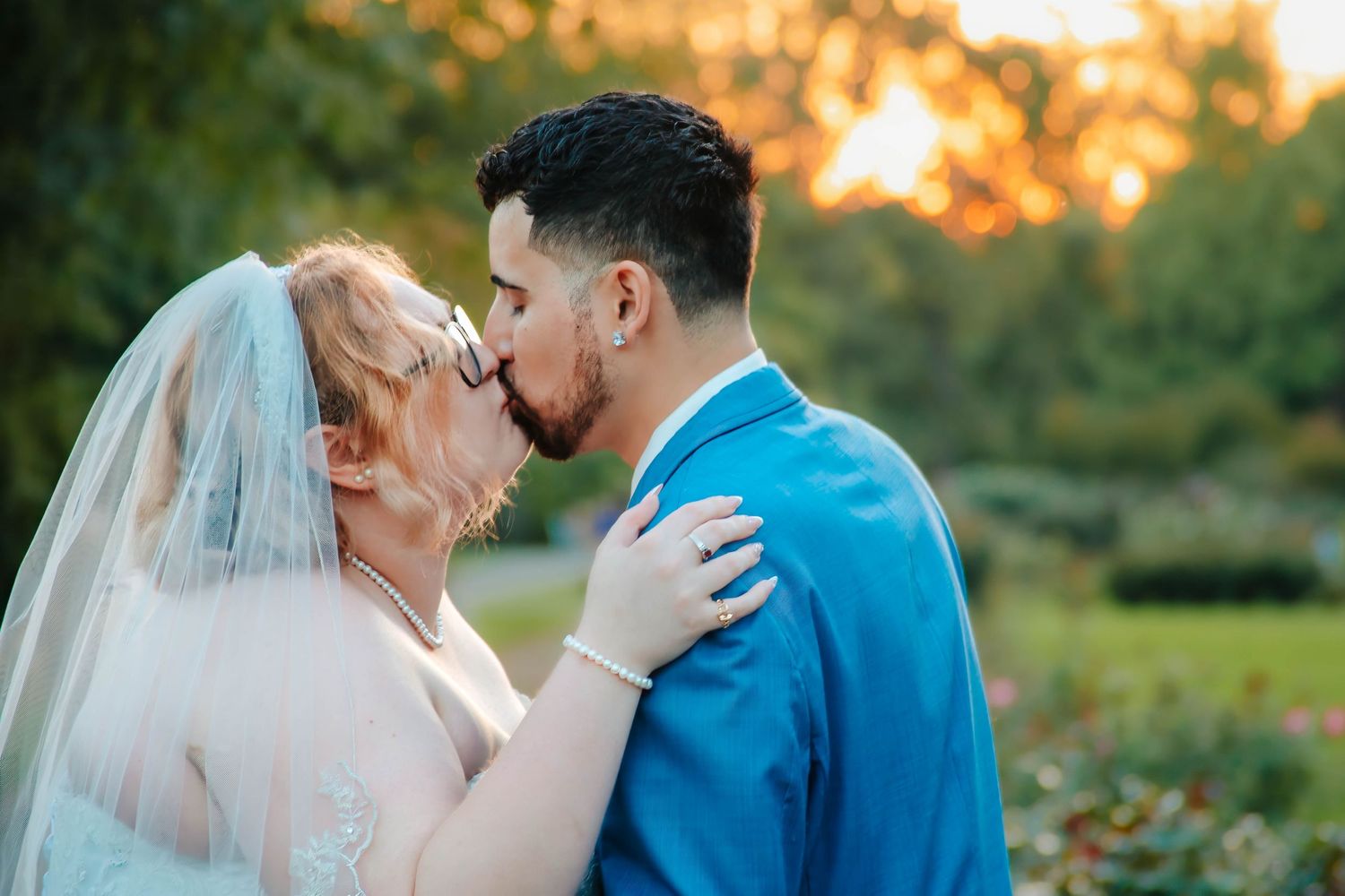 A romantic outdoor wedding photo of a couple kissing at sunset with the bride in white and groom in bright blue suit.