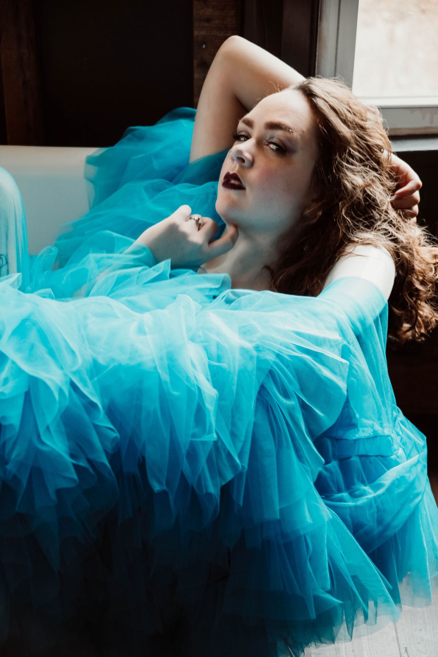 Dramatic boudoir photo with flowing turquoise tulle fabric against dark interior setting.