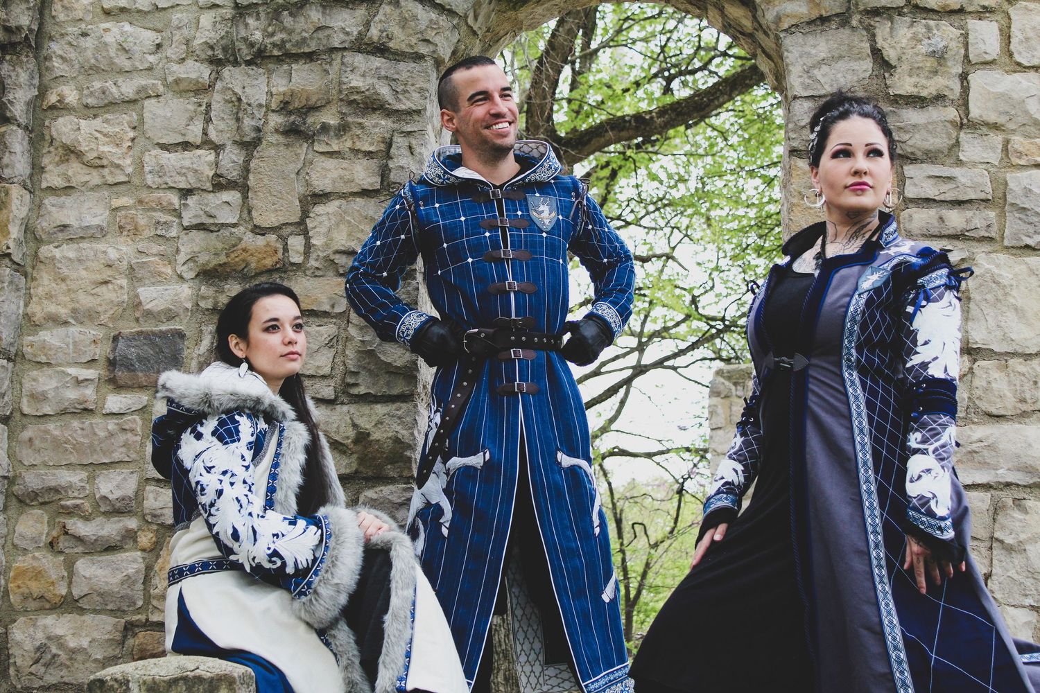 Group wearing Renaissance-style costumes posing against stone wall backdrop.