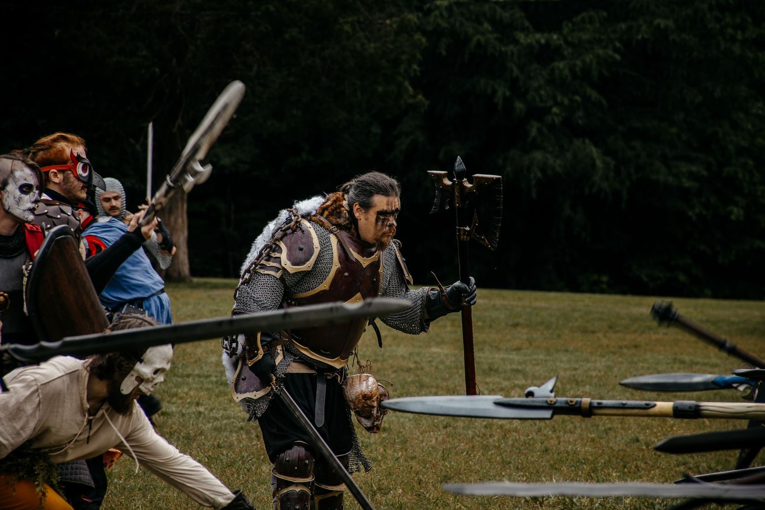 Medieval LARP battle reenactment with costumed warriors wielding spears and weapons in an outdoor field.