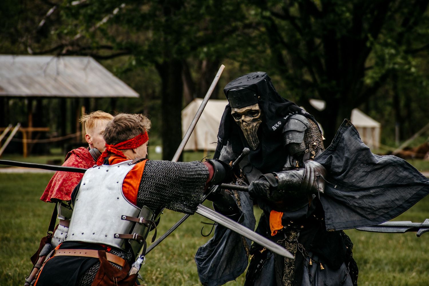 Two knights in medieval armor engage in a sword fight at a historical reenactment event outdoors.
