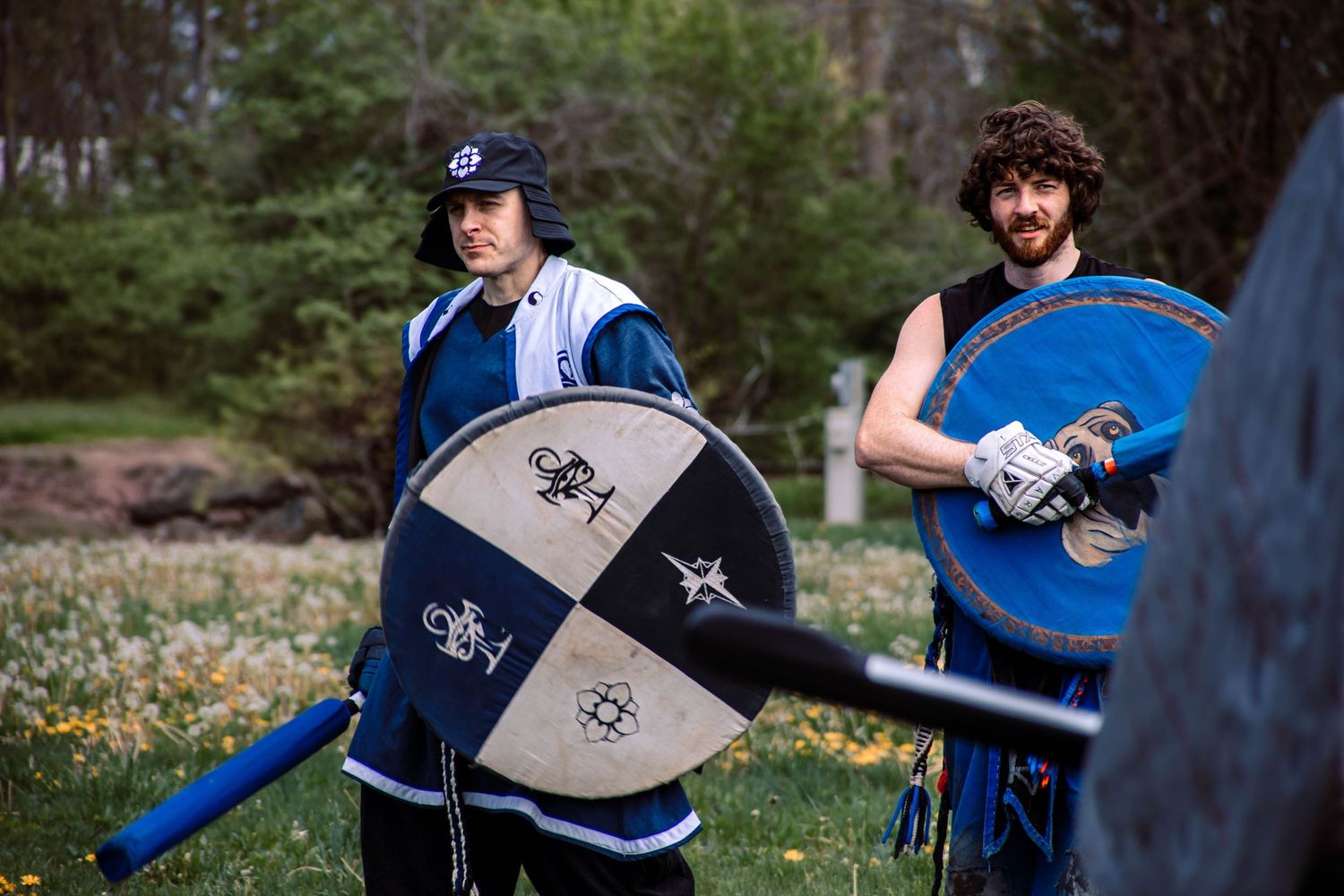Two people practicing sword fighting techniques with medieval-style weapons in an outdoor setting.