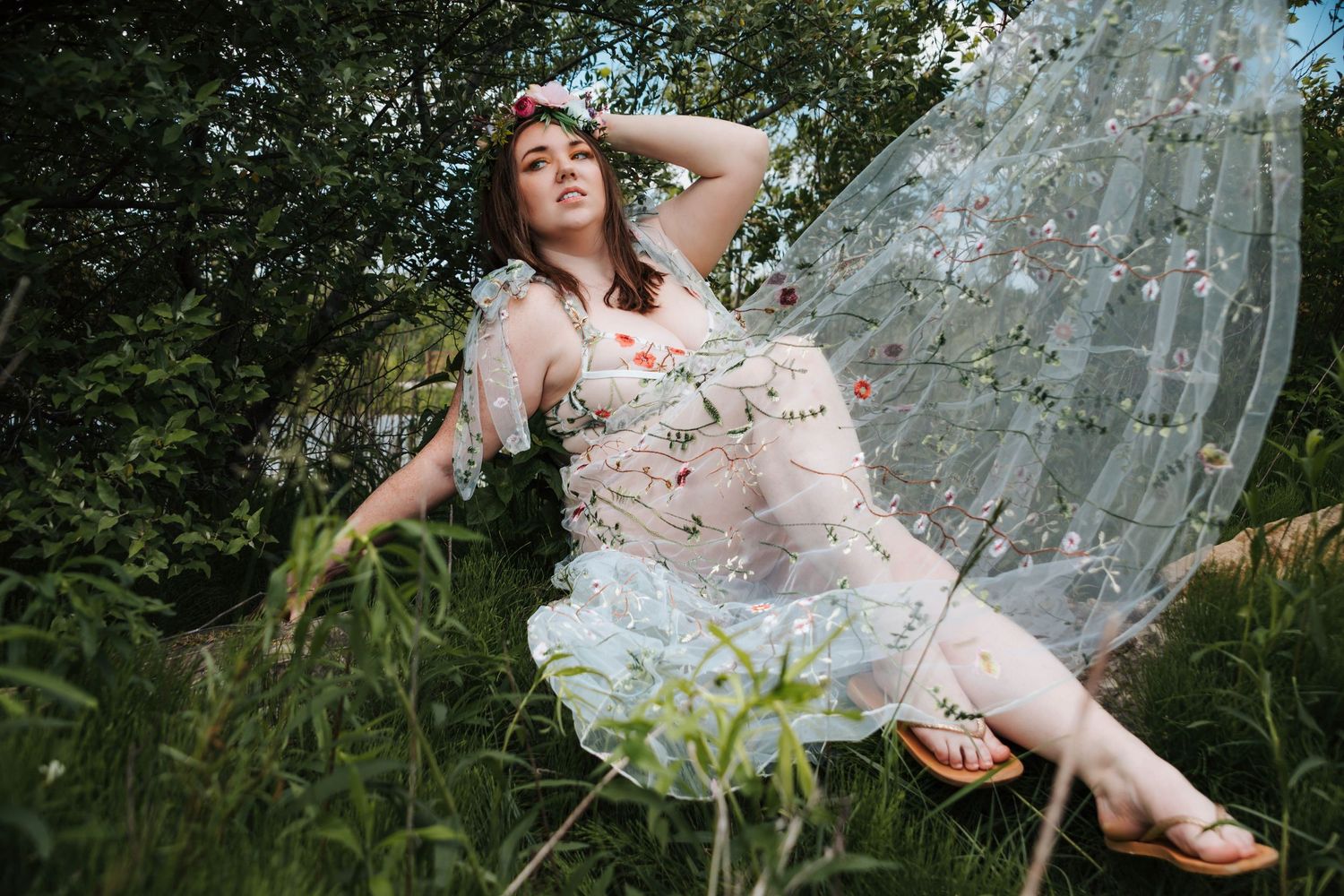 Dreamy outdoor portrait with floral dress and sheer overlay in natural setting.