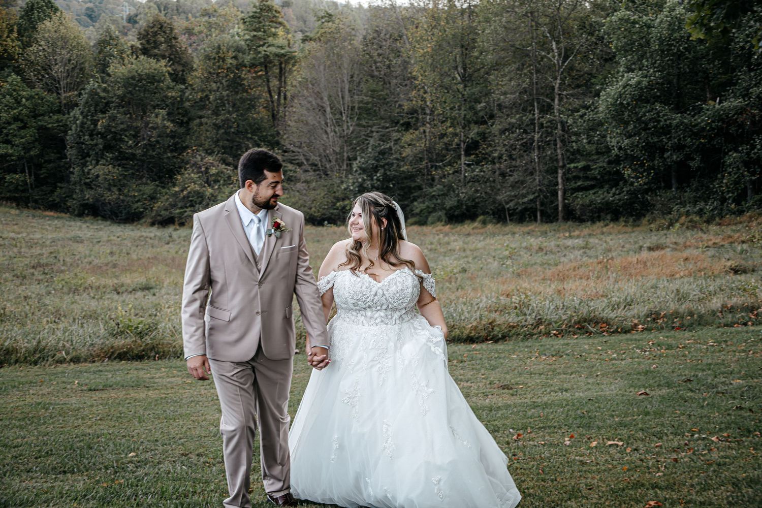 Wedding couple walking together across a grassy field in formal attire.