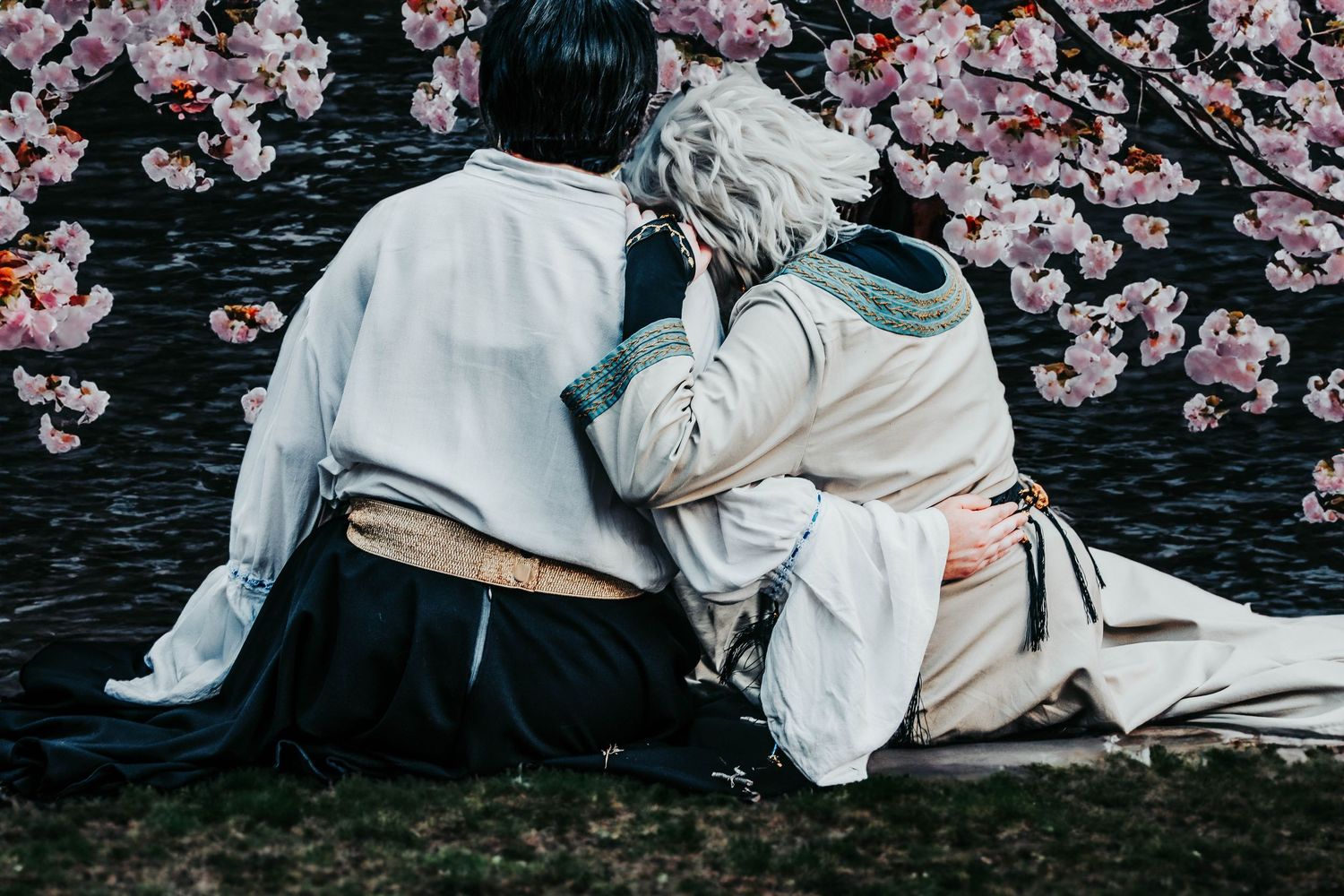 Cherry blossom petals frame a romantic scene in traditional Japanese clothing against a dark background.
