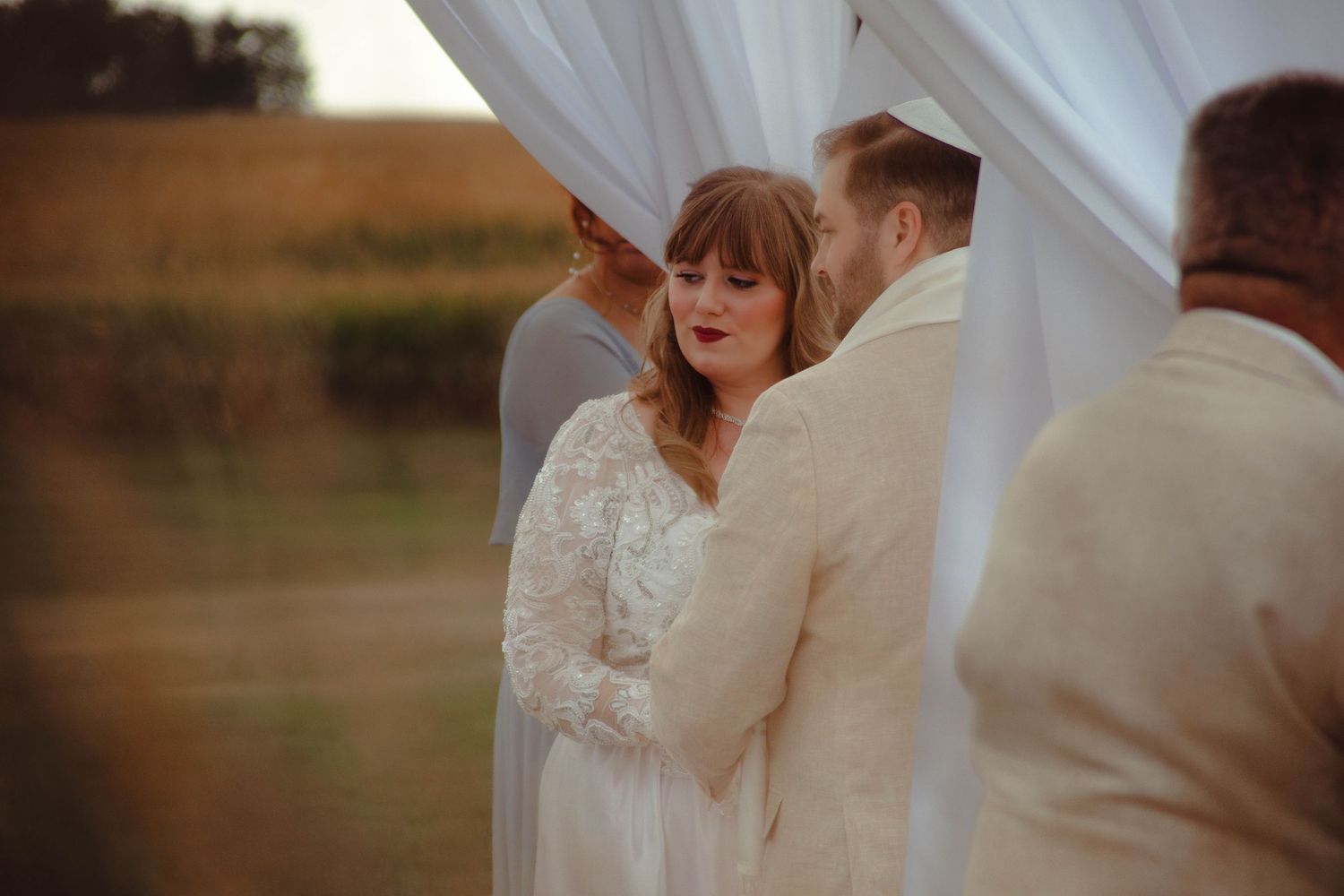 A couple celebrates their wedding day in a rustic outdoor field setting during golden hour with flowing white dress details.