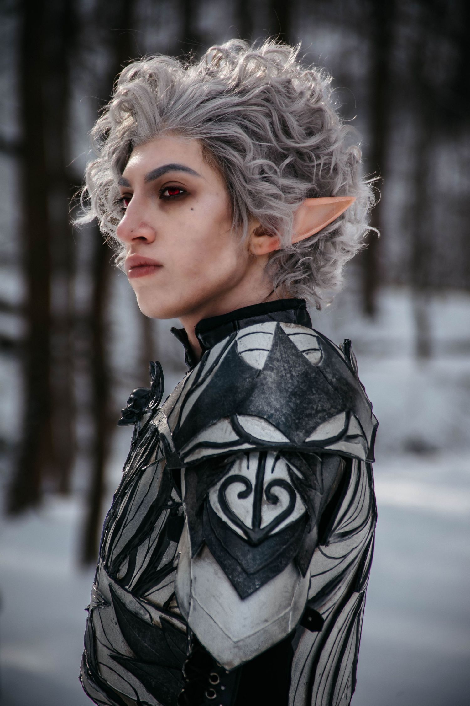 Fantasy elf cosplay character with silver hair and dark makeup in winter forest setting.