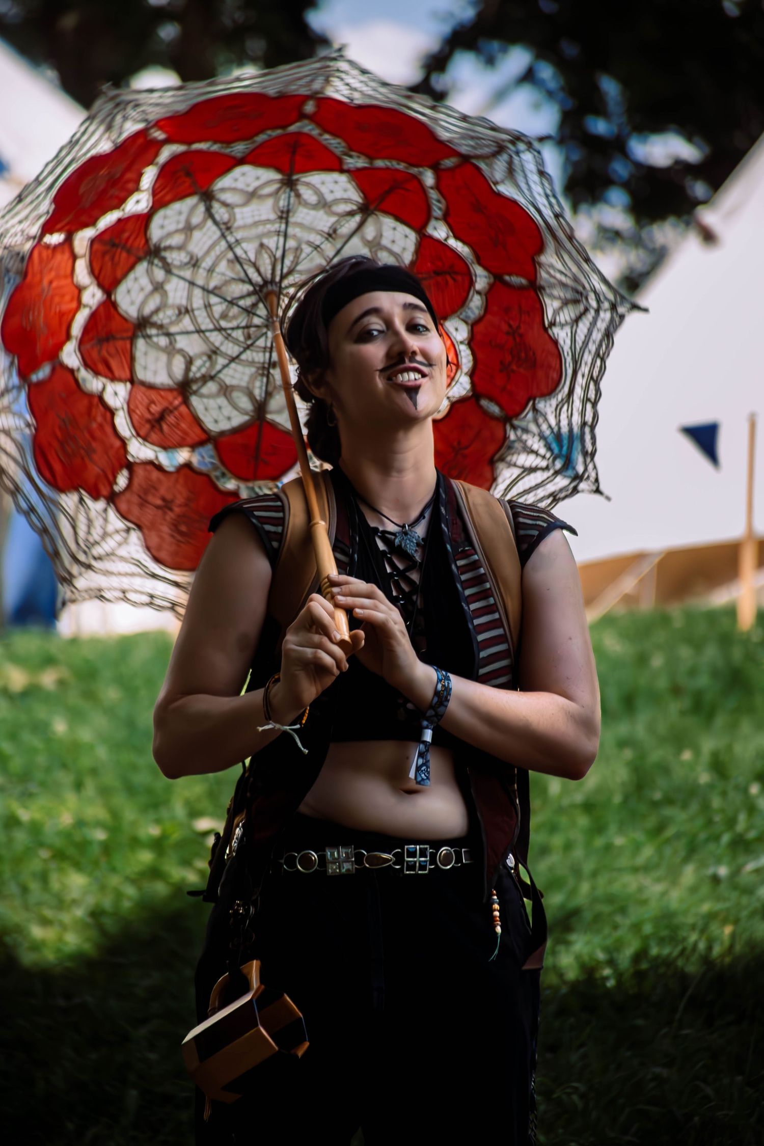 Someone holds a decorative red and white lace parasol while wearing alternative style clothing at an outdoor festival.