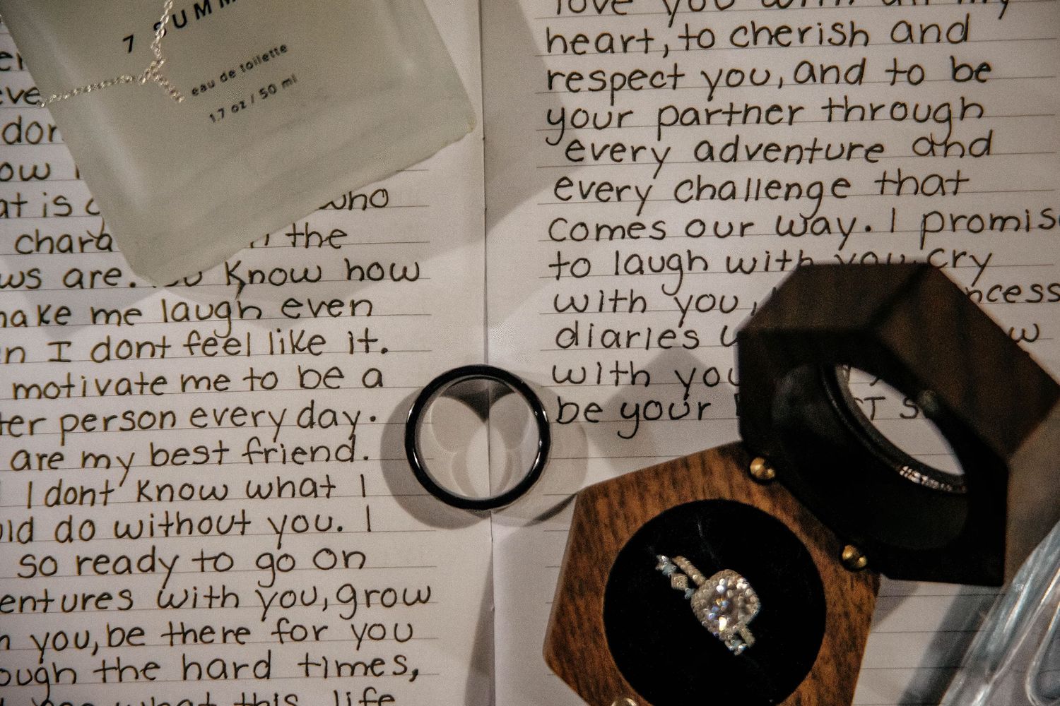 Handwritten love letter with engagement ring and black ring box on white surface.