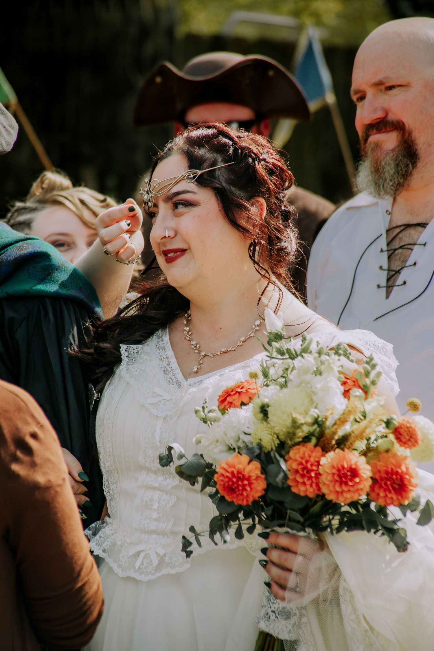 Couple sharing a joyful moment at outdoor wedding ceremony with orange dahlia bouquet and white attire.