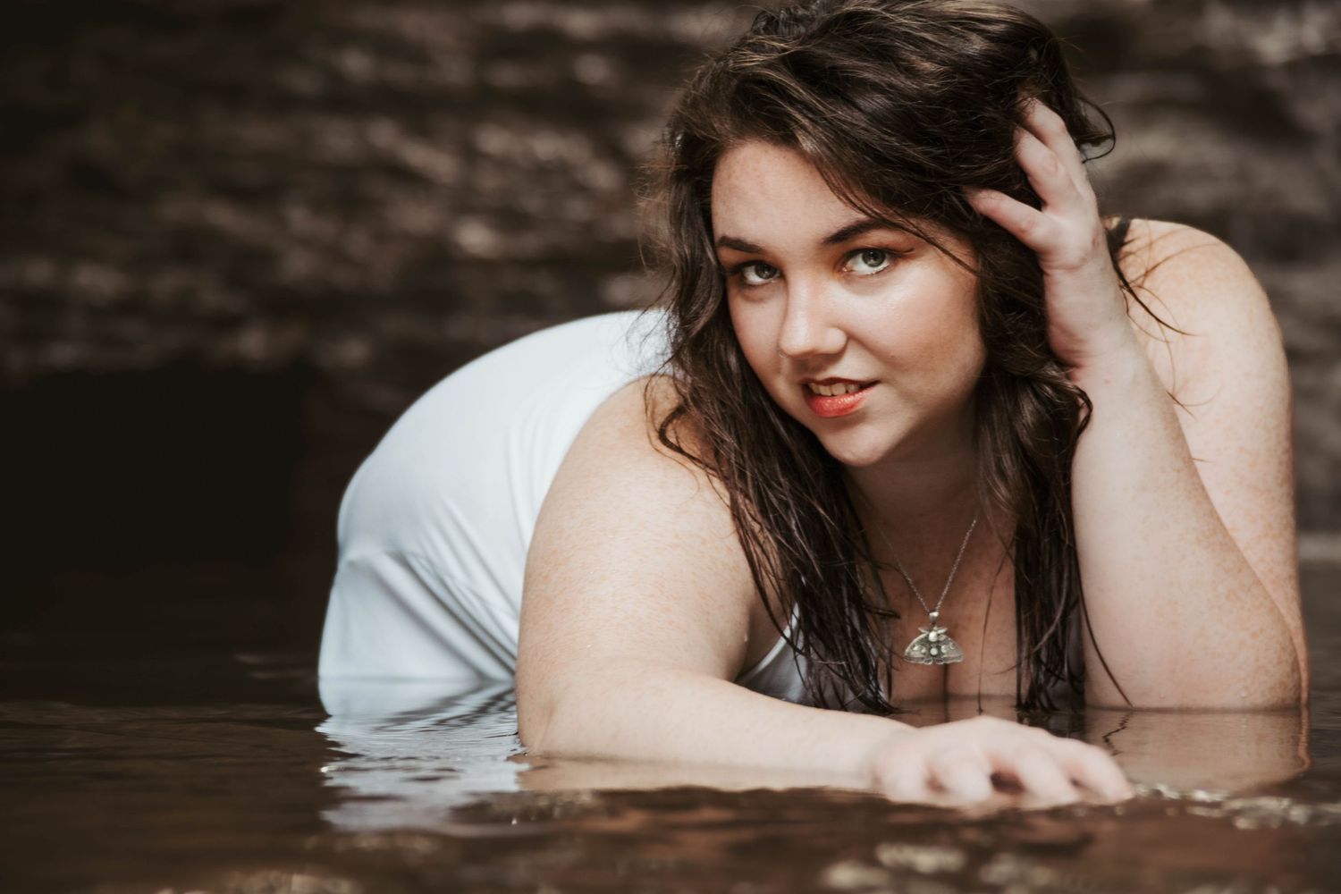 Artistic portrait in water with natural lighting and rustic rock wall backdrop.
