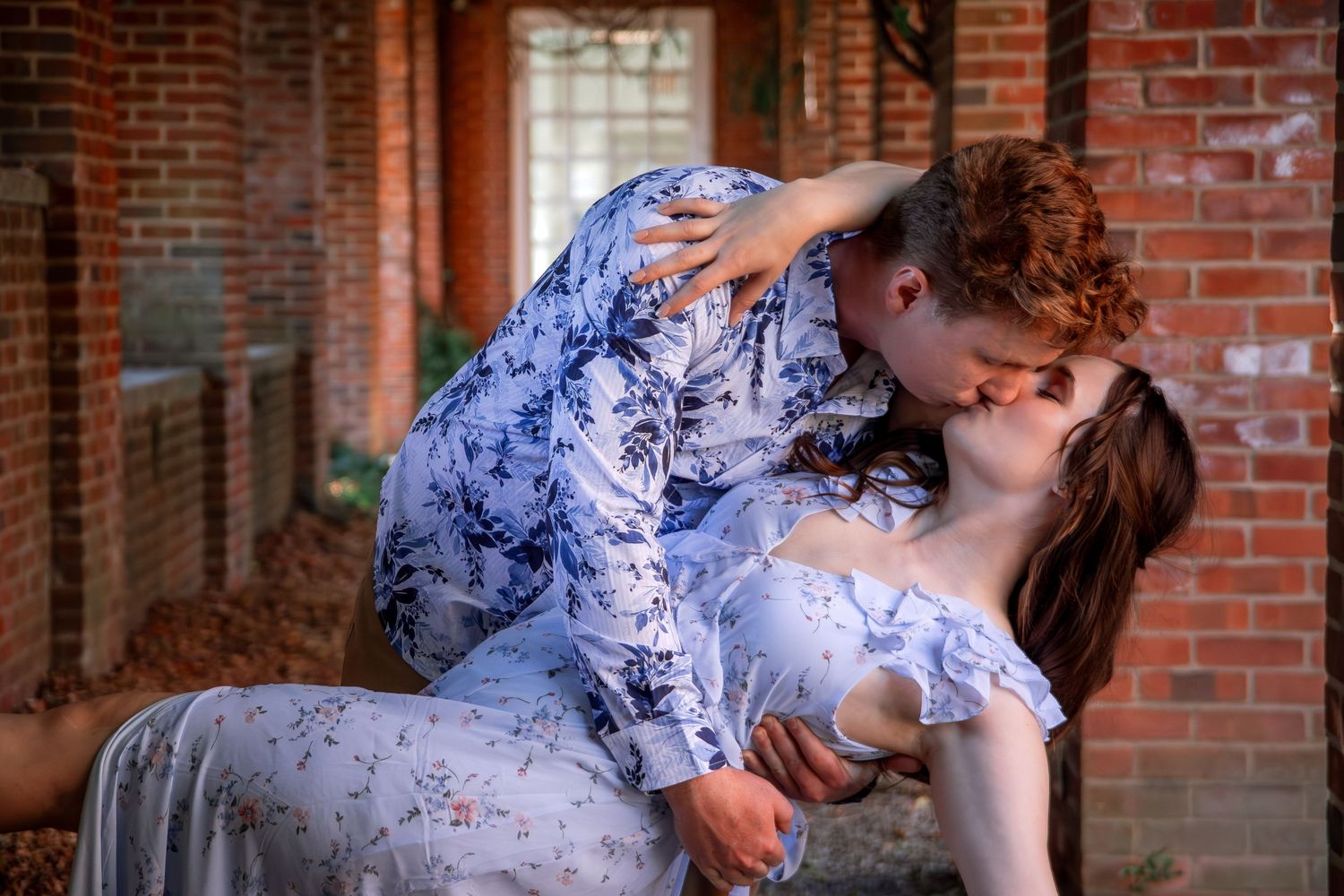 Romantic couple poses against rustic brick wall backdrop in coordinated outfits.