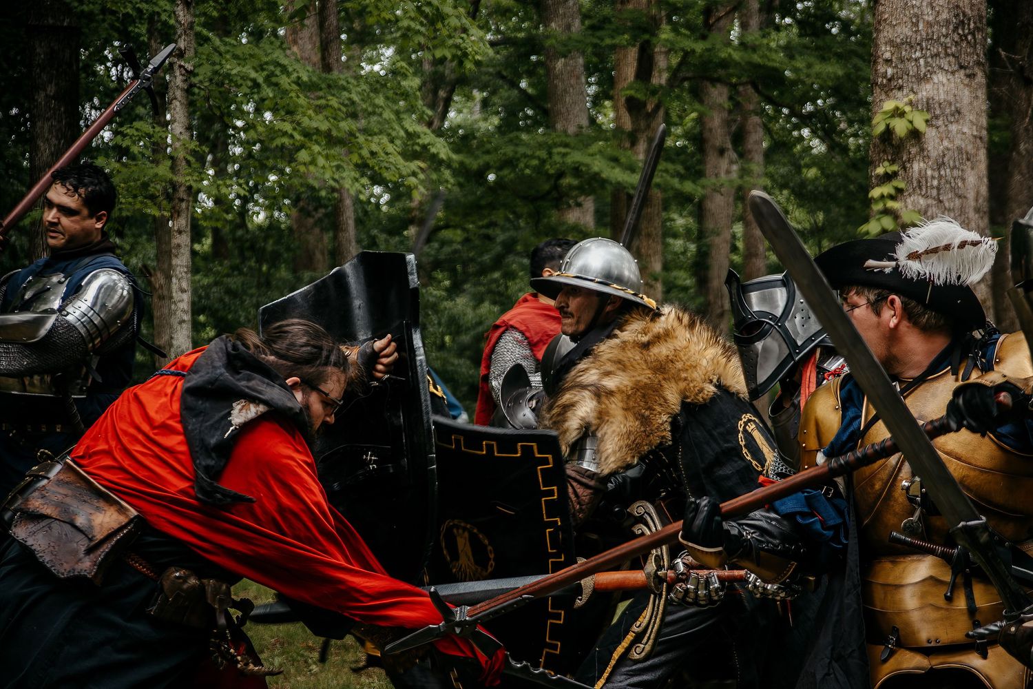 Medieval battle reenactment with warriors in armor and red capes fighting in a forest setting.