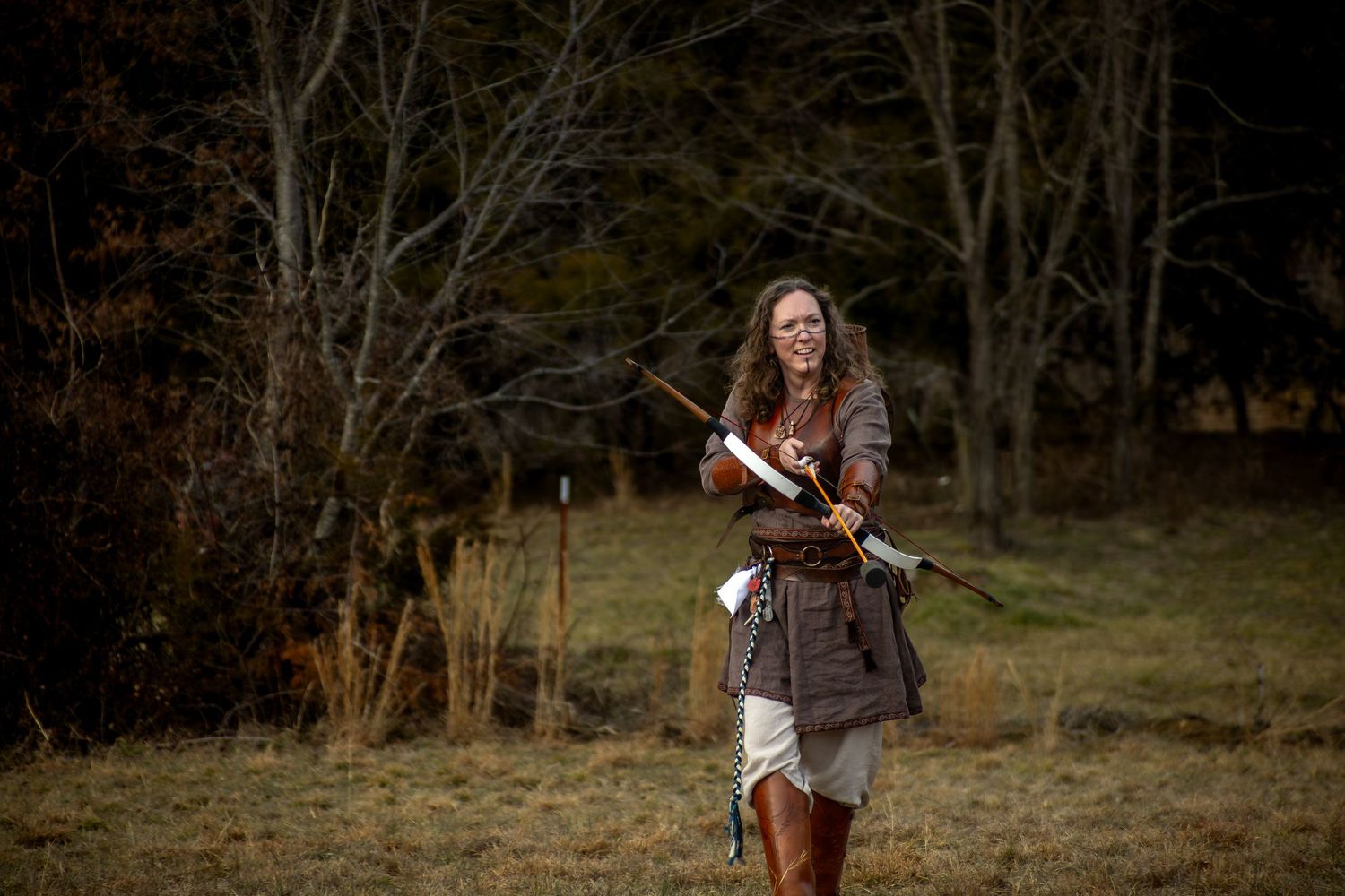 A violinist plays their instrument in a rustic outdoor setting during autumn with bare trees in the background.