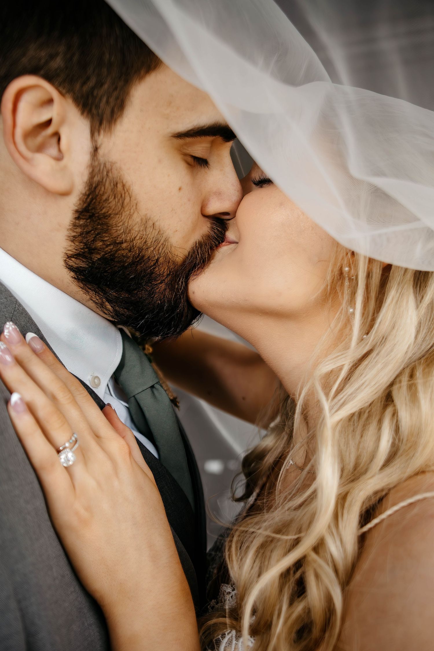 A romantic close-up of a couple sharing a tender kiss, with the bride's blonde hair and engagement ring visible.