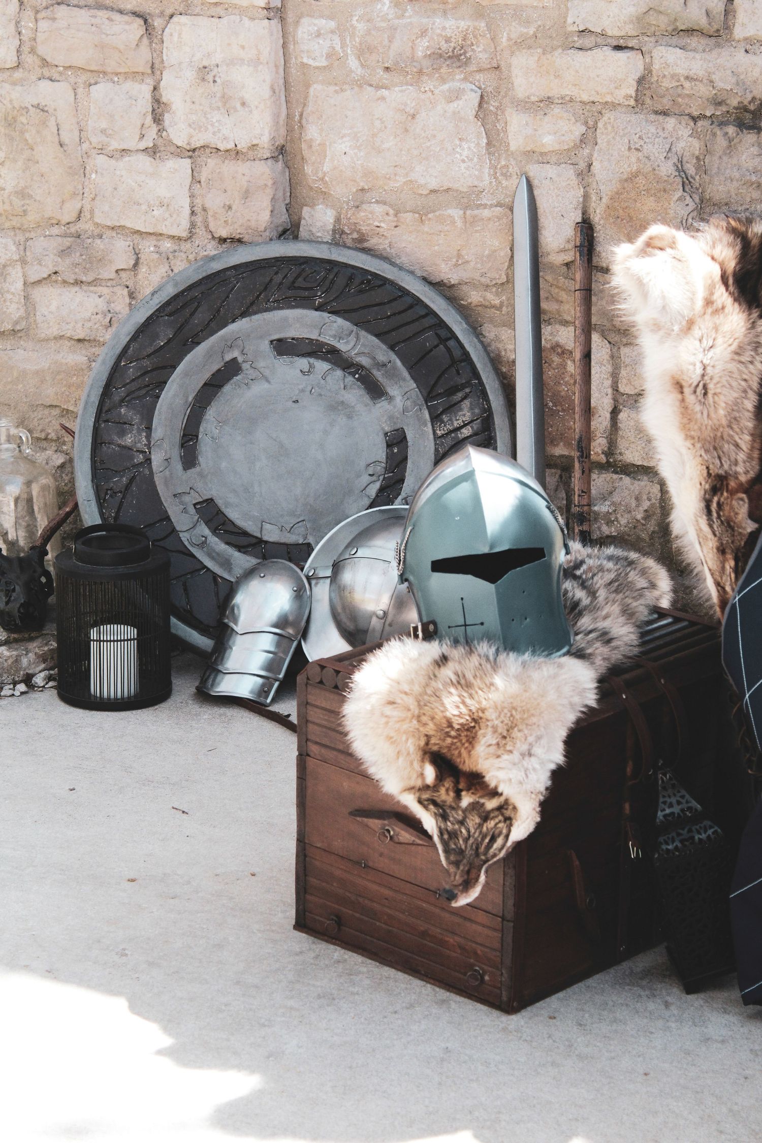 Medieval knight armor props and accessories displayed against stone wall with wooden box and decorative elements.