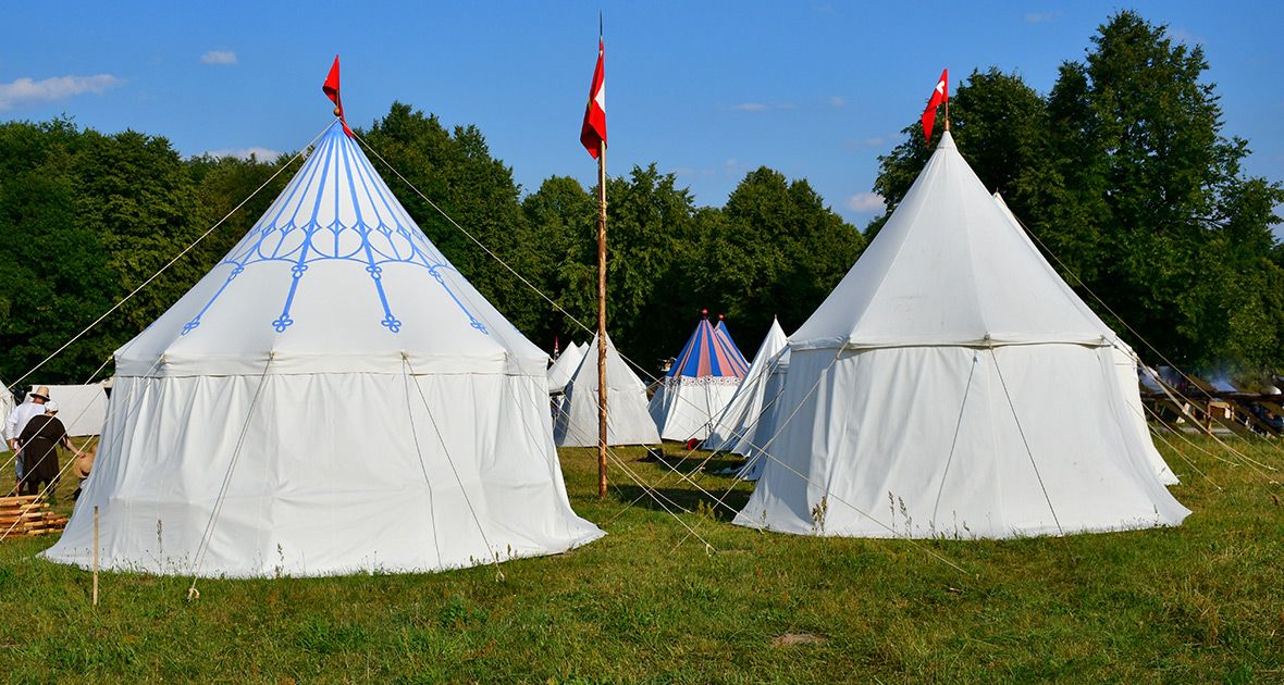 White medieval style canvas tents with red flags displayed at a historical reenactment camp on grassy field.