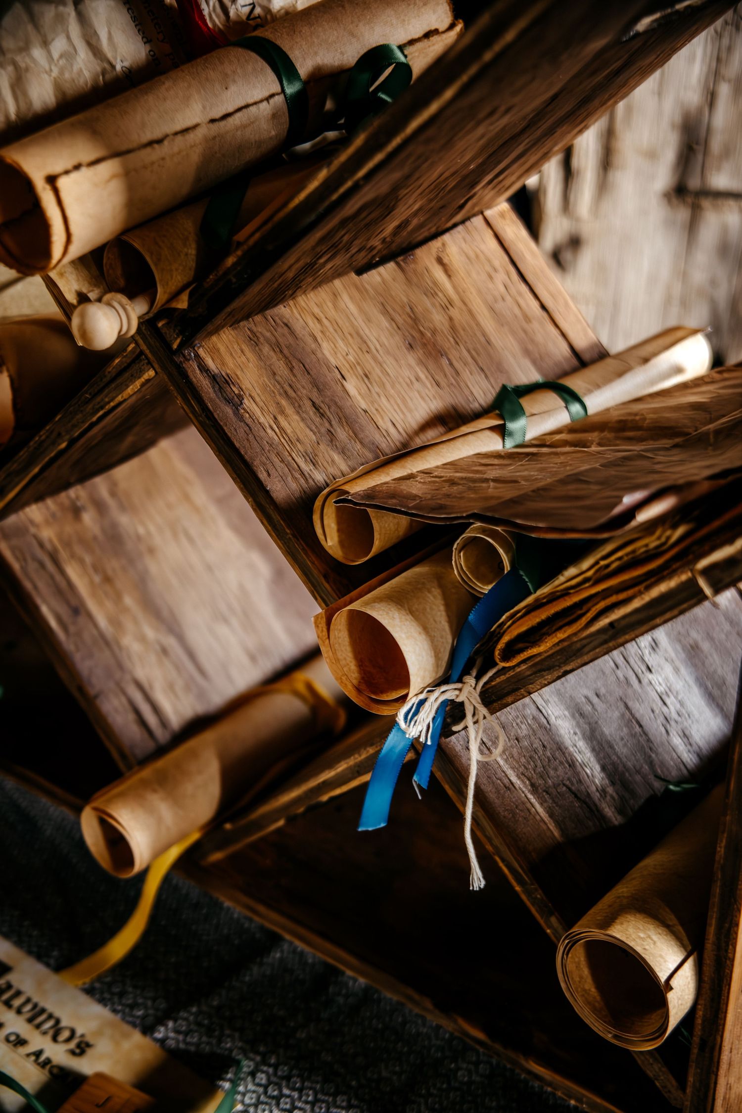 Antique parchment scrolls tied with colorful ribbons rest on rustic wooden shelves in a vintage library setting.
