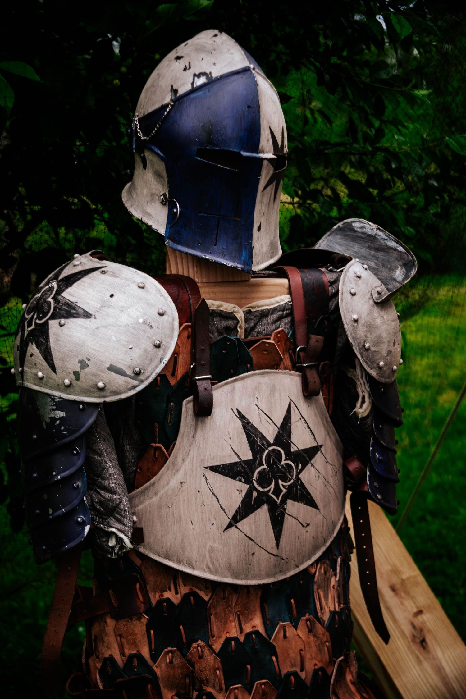 Medieval knight armor with black star emblem displayed against green foliage background.